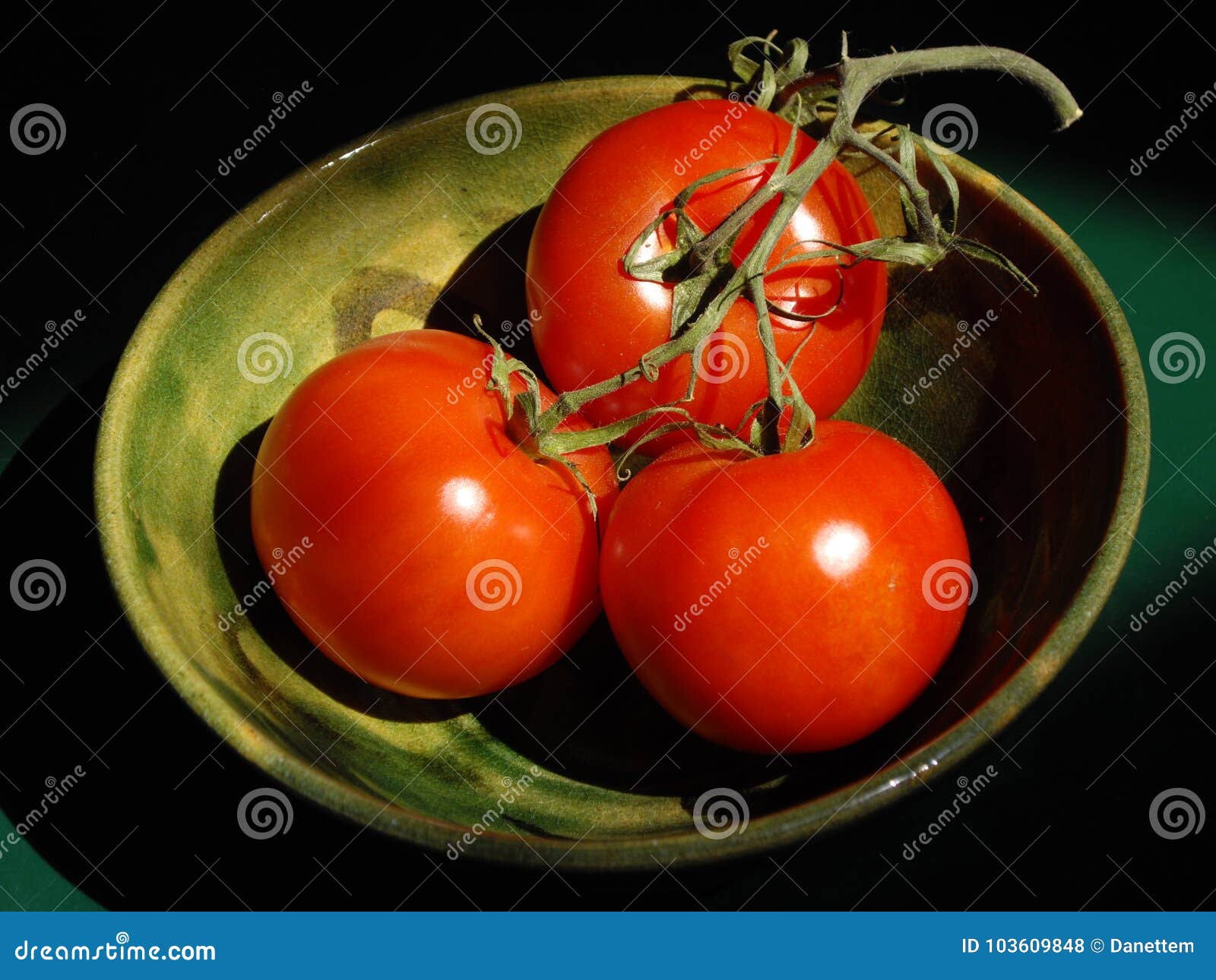 Ciotola di pomodori fuori dalla vite. Una ciotola ceramica verde con tre pomodori rossi maturi fuori dalla vite