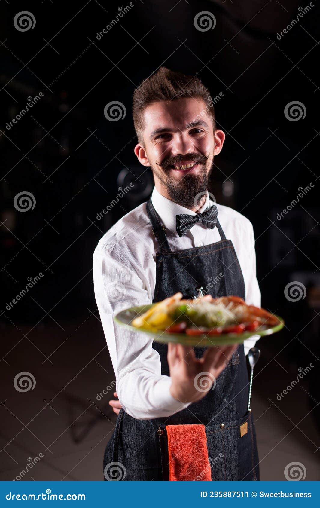 professional garcon holds salad on a black background.