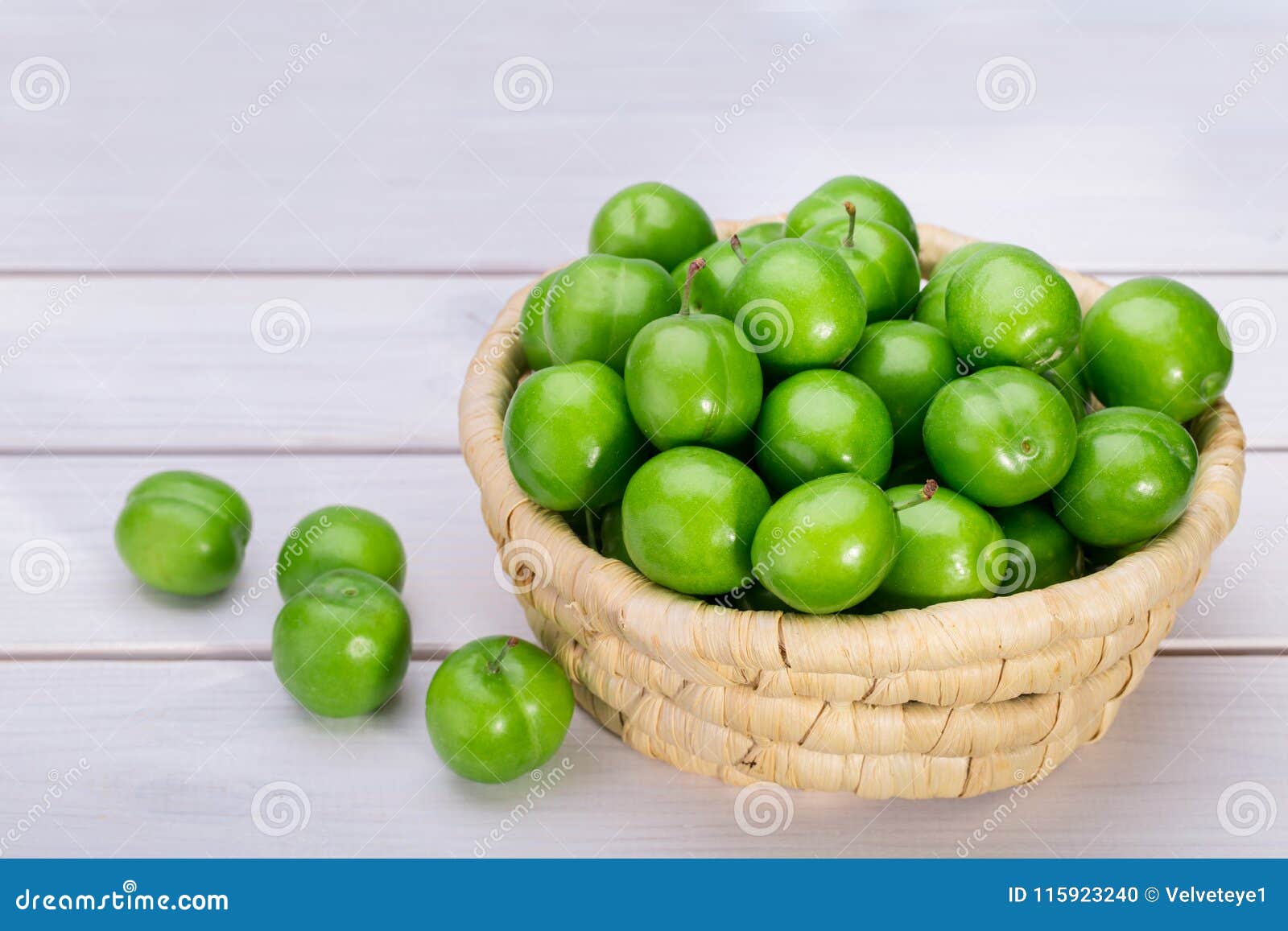 Ciérrese para arriba de ciruelos o de la ciruela claudia verdes en una cesta aislada en Whi. Ciérrese para arriba de ciruelos o de la ciruela claudia verdes en una cesta aislada en el fondo de madera blanco, frutas populares de la primavera con un gusto amargo muy agudo originado en Irán