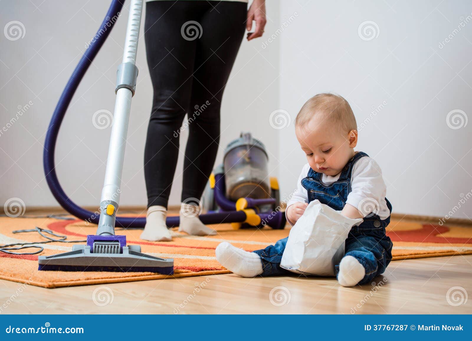 Cleaning home - mother and child. Cleaning up the room - women with vacuum cleaner, baby sitting on floor