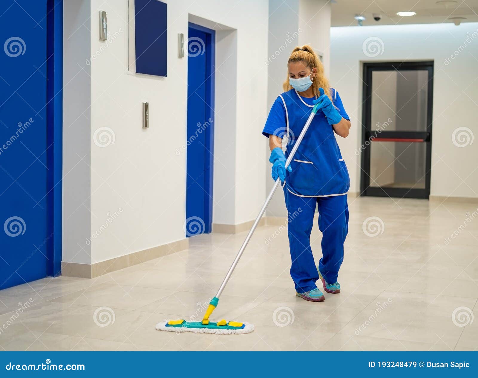 a cleaning lady with a mask on her face cleans the hallway
