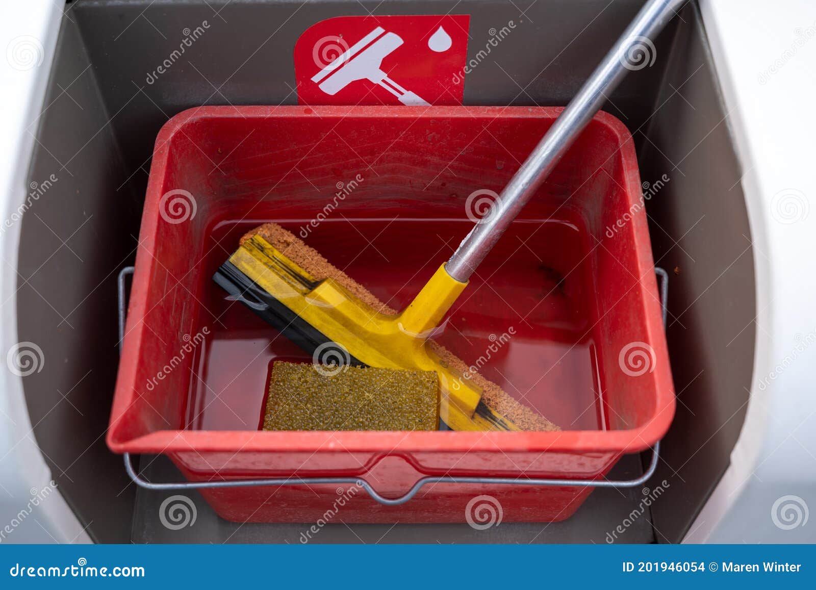 cleaning set with squeegee, sponge and water for car windscreens in a red bucket at a gas station