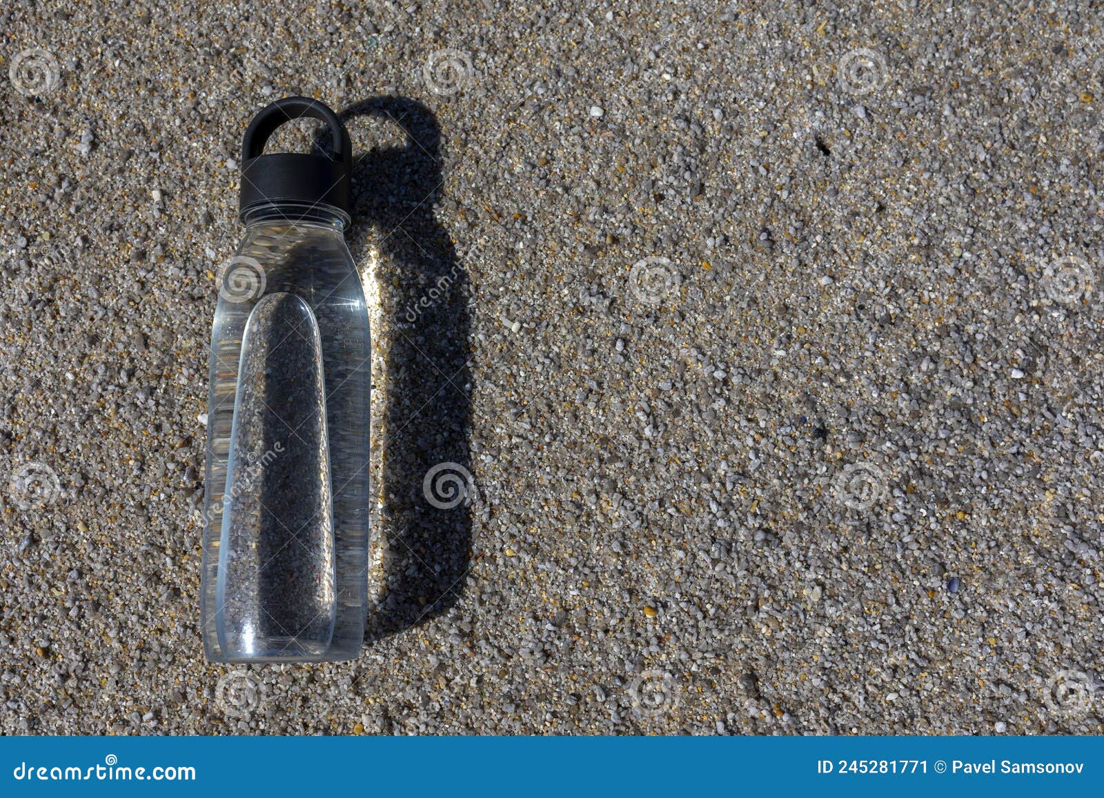 a clear bottle of water lies on the sand.
