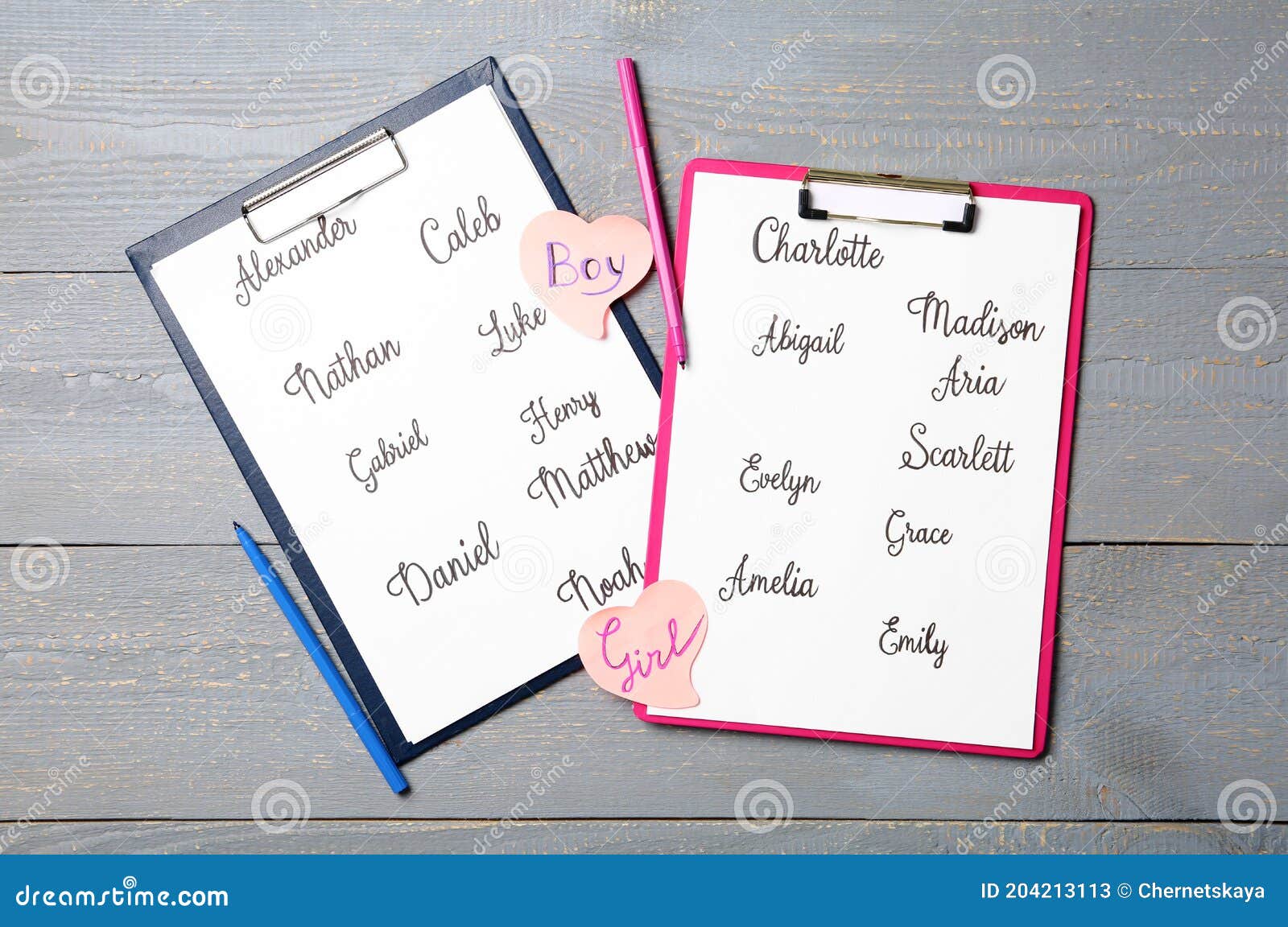 clipboards with different baby names and felt tip pens on grey wooden table, flat lay