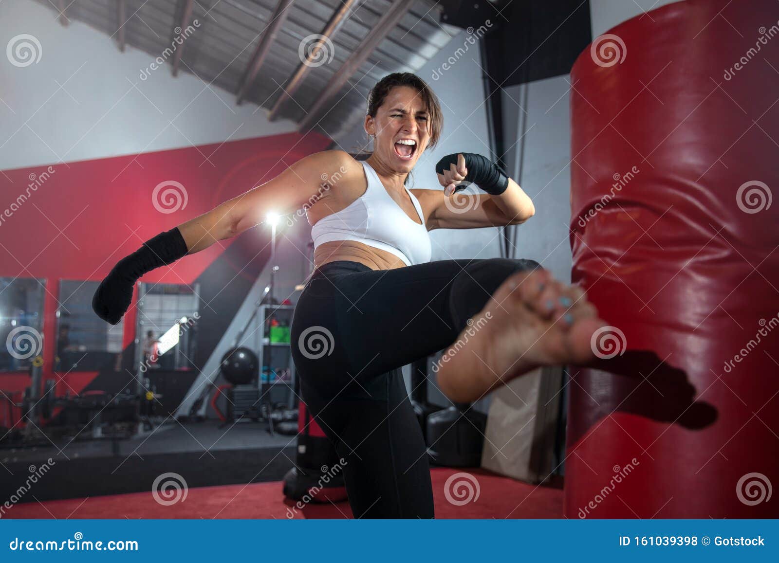 close up action lifestyle portrait of an active sweaty athletic female mma fighter kicking a bag, gym training, self defense and e