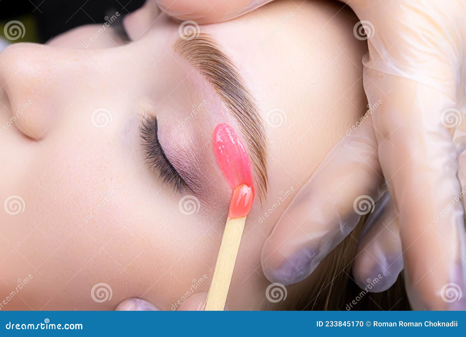 close-up of applying red wax to remove unwanted hairs from the lower contour of the model`s eyebrows