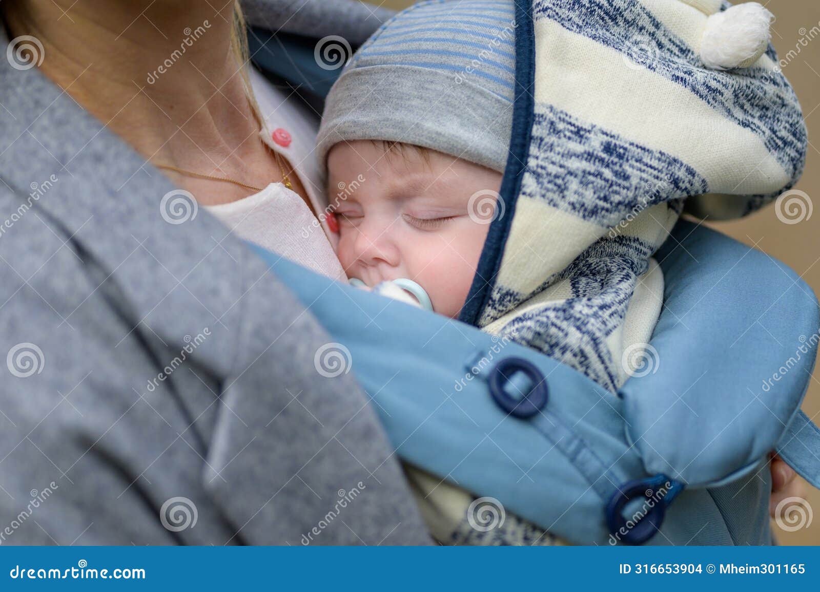 close up of a baby sleeping in a baby carrier on his mother's chest or cleavage, in an exceptionally intimate closeness