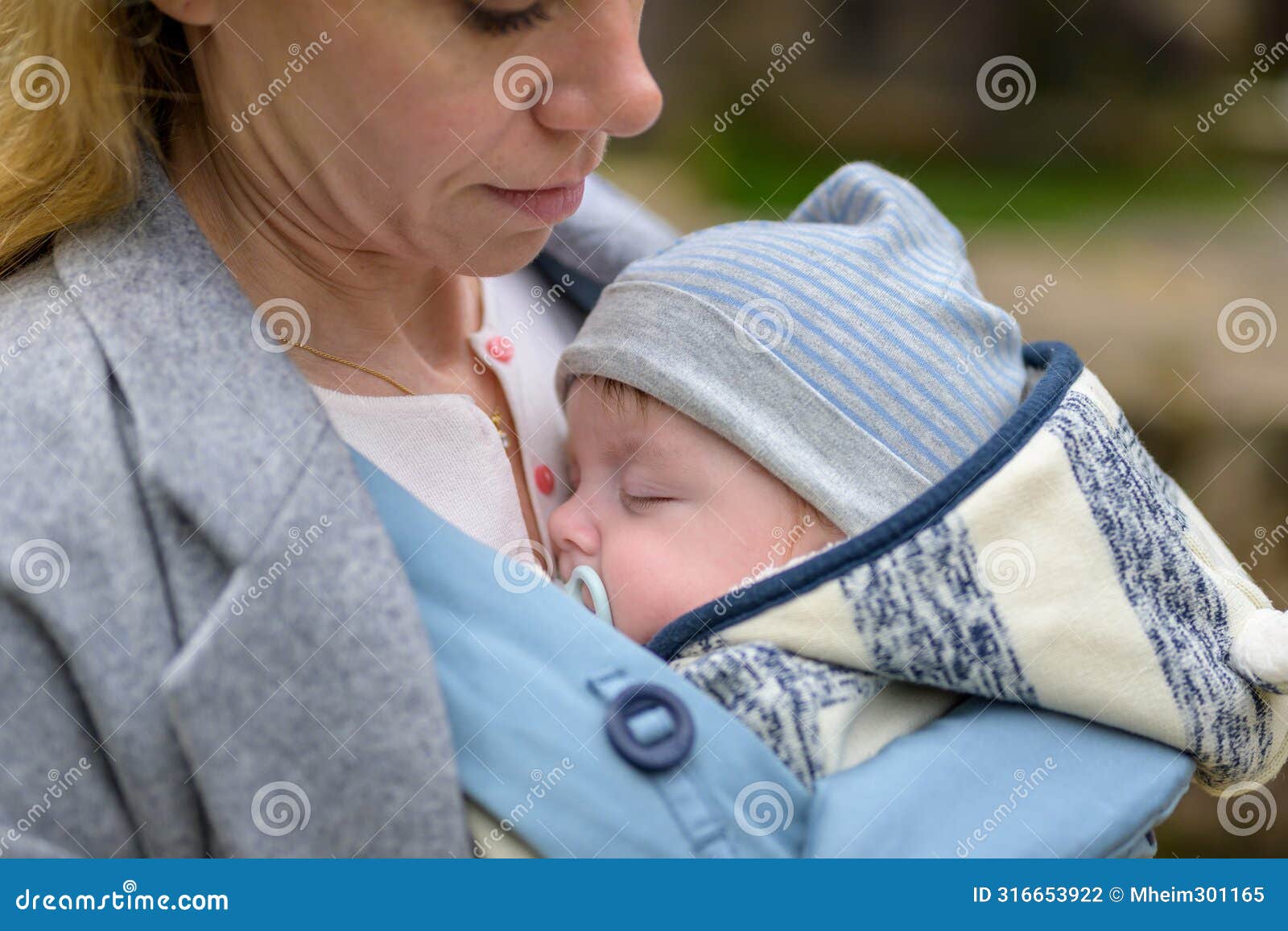 close up of a baby sleeping in a baby carrier on his mother's chest or cleavage, in an exceptionally intimate closeness