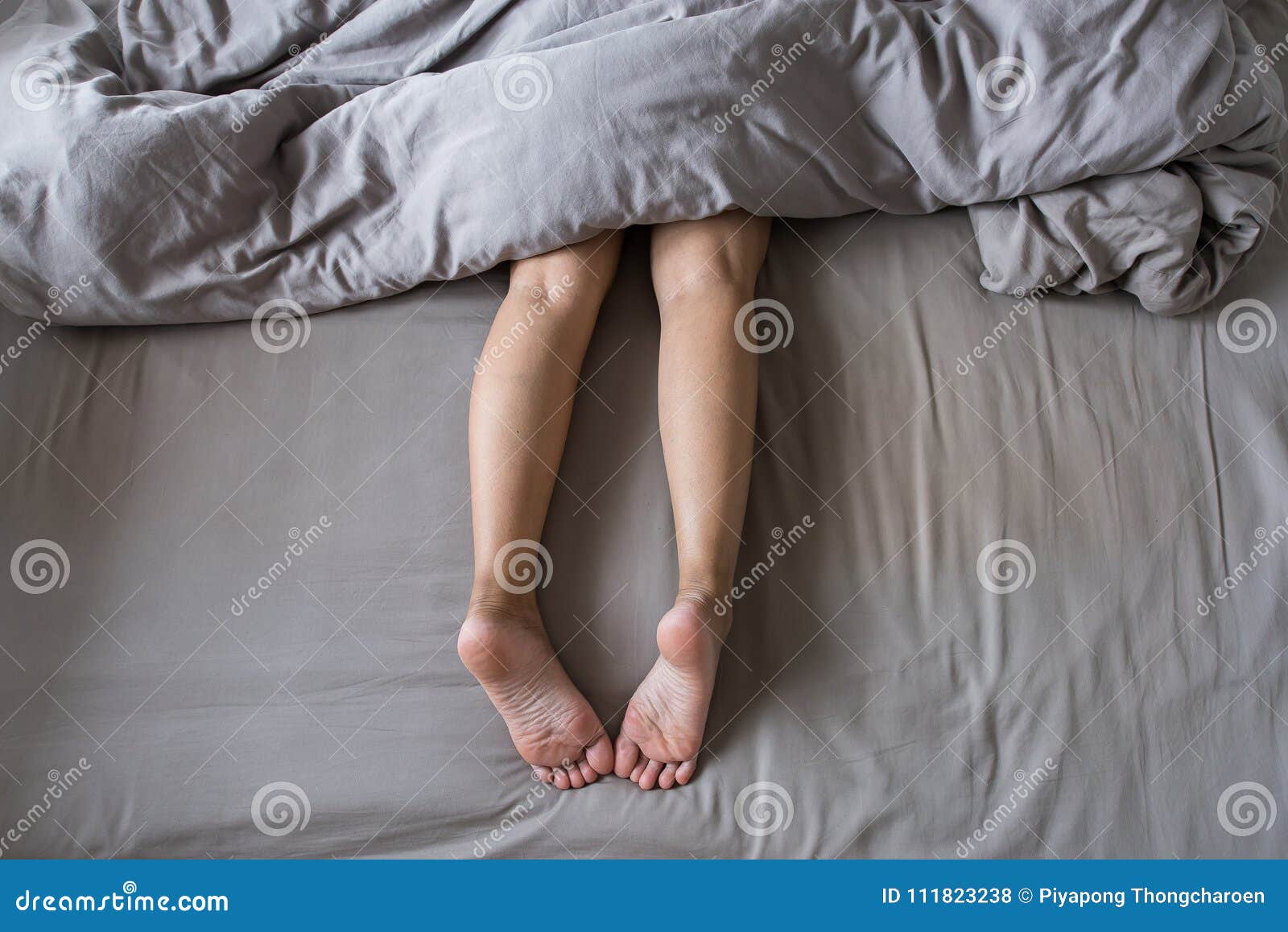 Close Up of Barefoot and Leg Under Blanket on the Bed Stock Photo