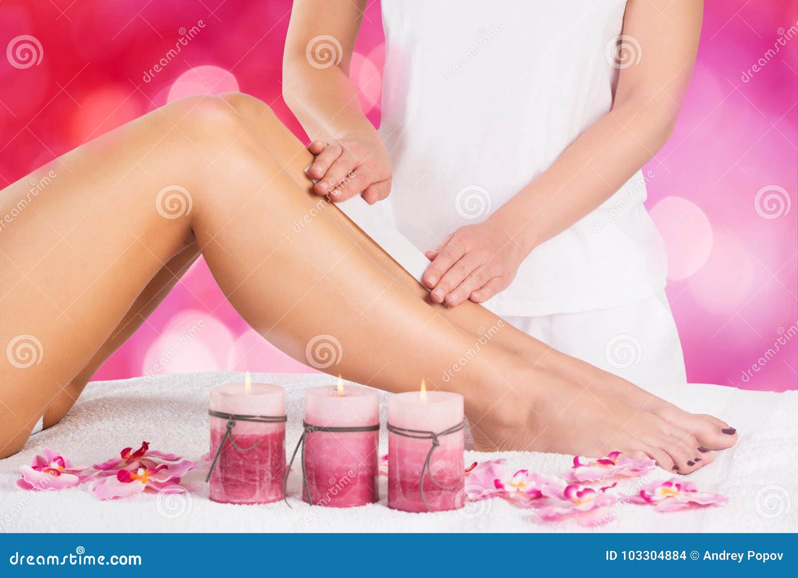 beautician waxing leg of woman with wax strip