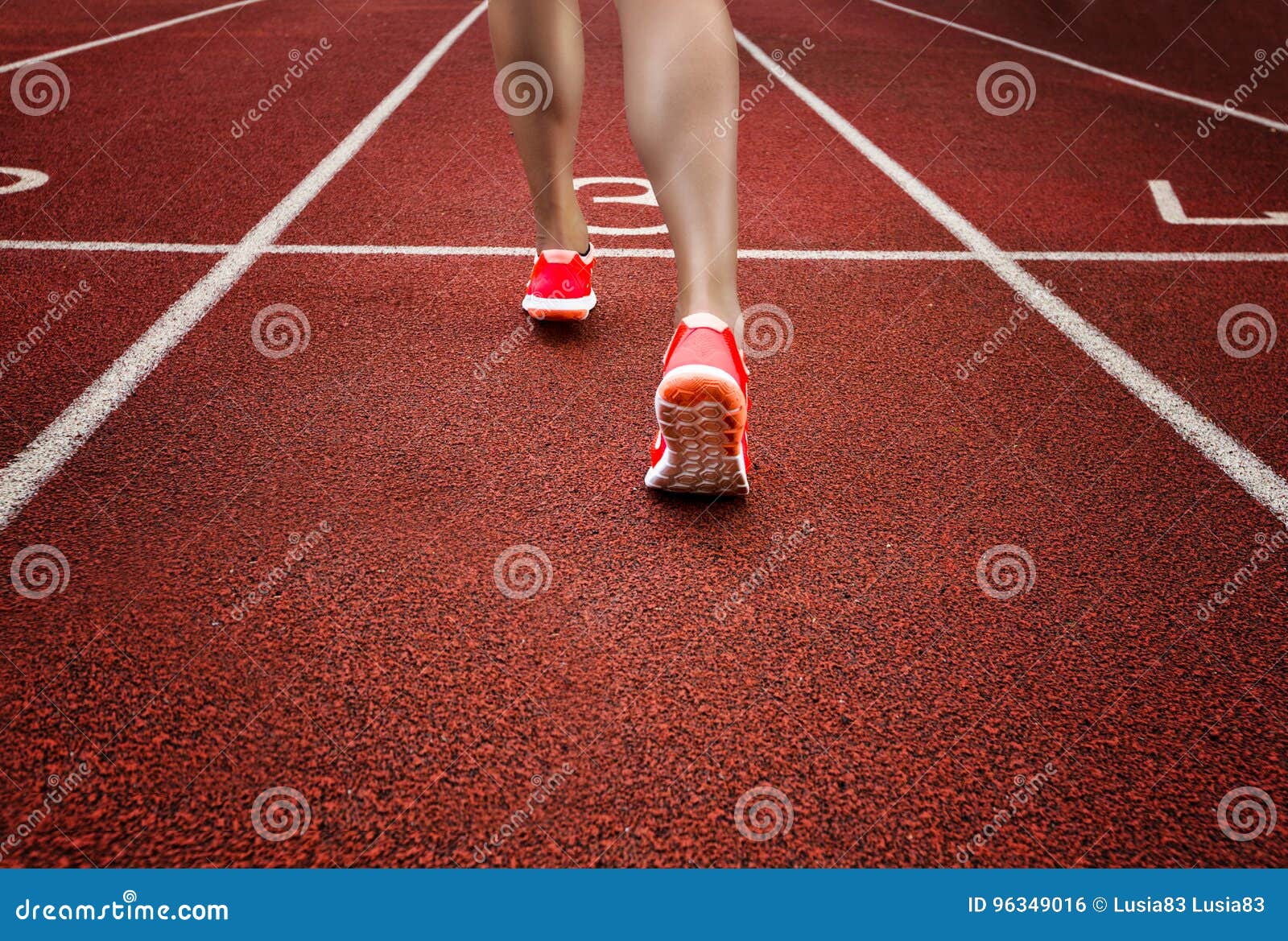 Close up on beautiful female legs with pink shoes on the running track. Red running track with female runner