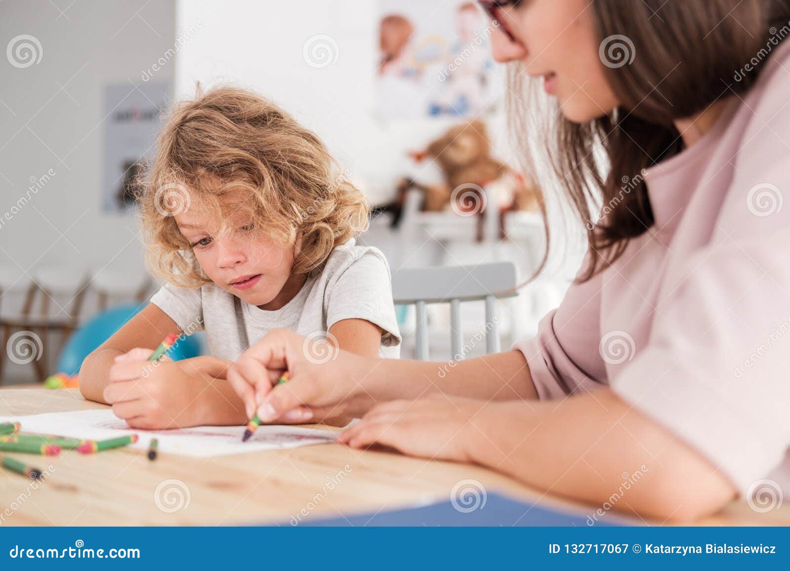 child with an autism spectrum disorder and the therapist by a table drawing with crayons during a sensory