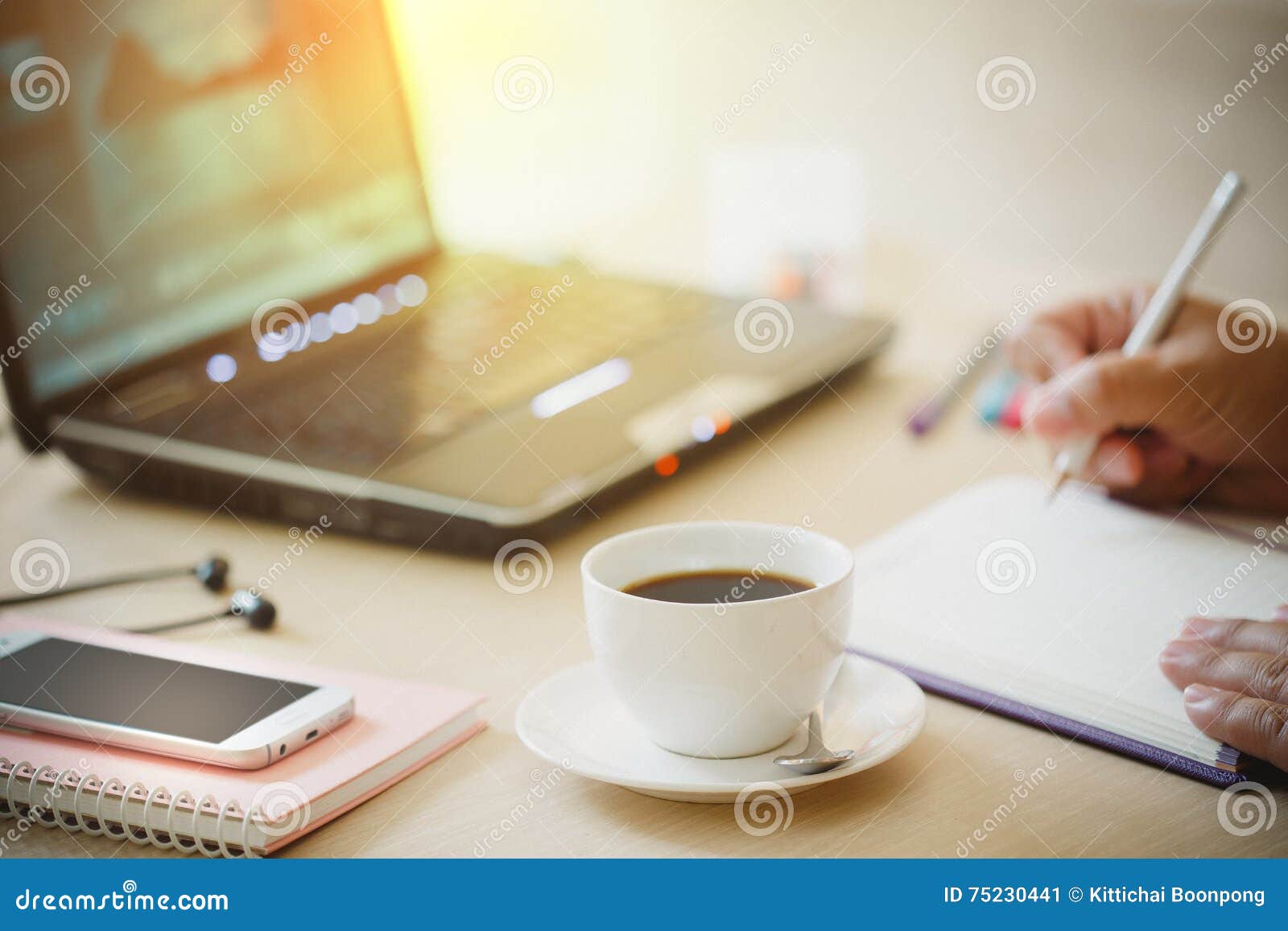 close up cup of coffee and smart phone with hand of business man using laptop computer and write notebook on wooden desk office w