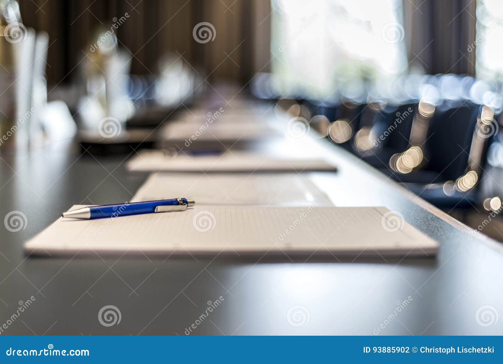 close up of dark conference table water glasses pens, paper sheets and blurry window background