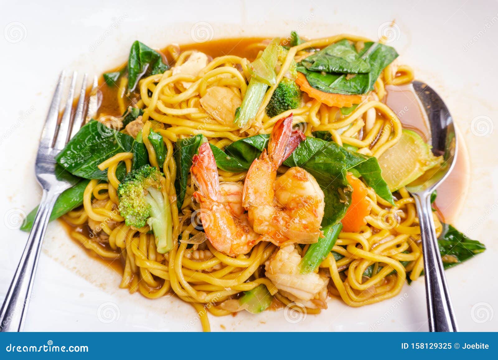 close up delicious yellow fried noodles with soy sauce, prawns, vegetables and mushrooms on the white plate background. thai stir-