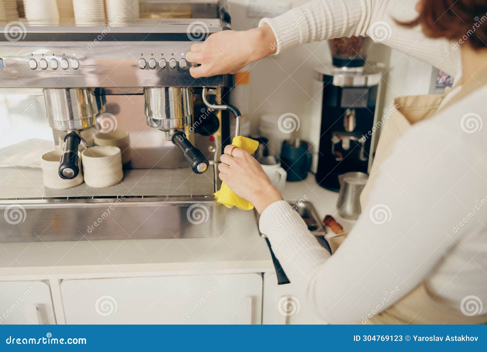 close up of female barista cleaning coffee machine at coffee shop after froths milk