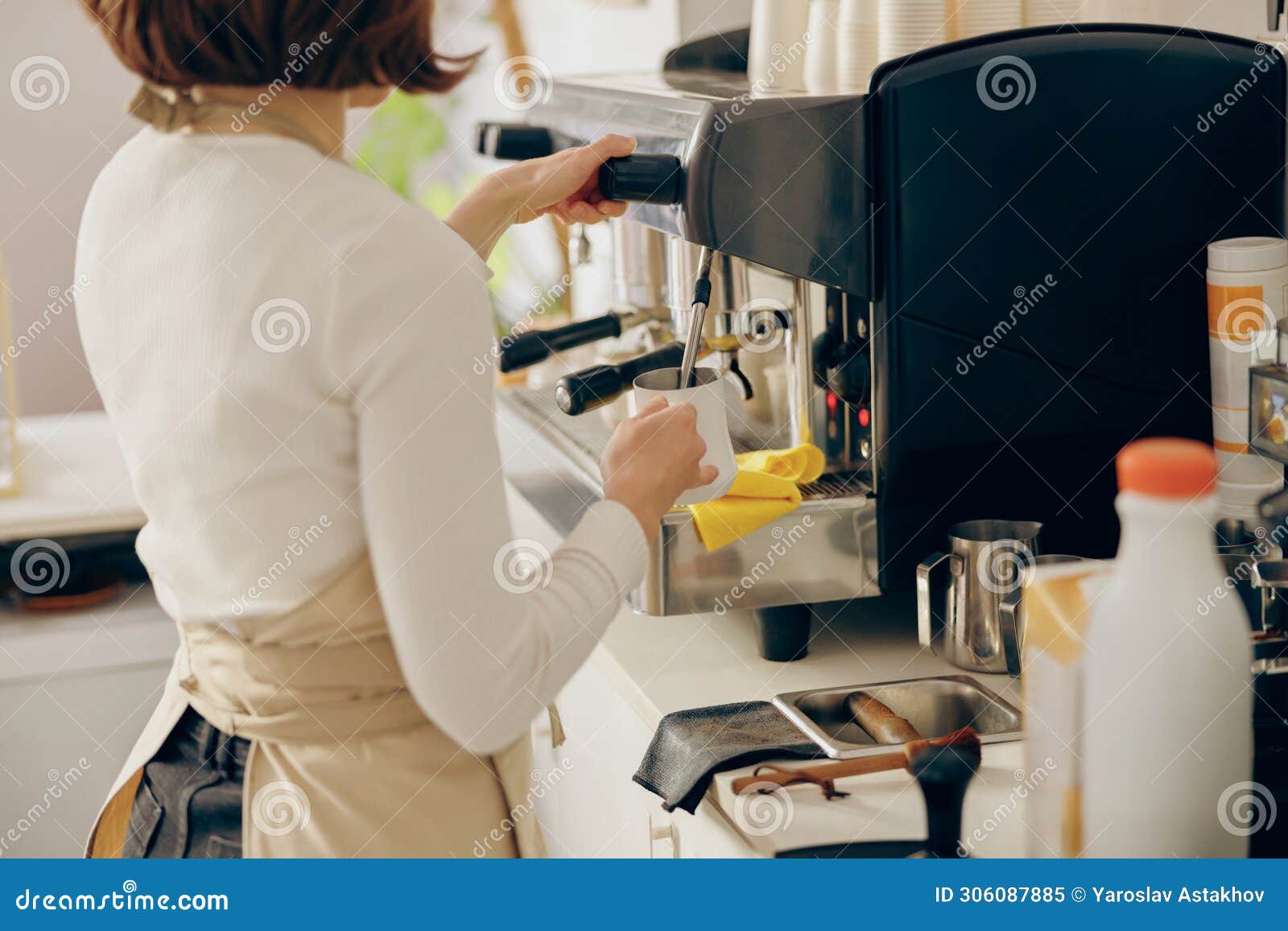 close up of female barista froths milk on a coffee machine for making cappuccino or latte