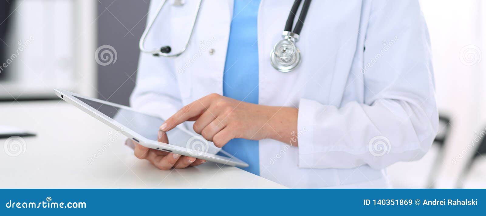 unknown doctor woman at work. female physician using digital tablet while standing near reception desk at clinic or