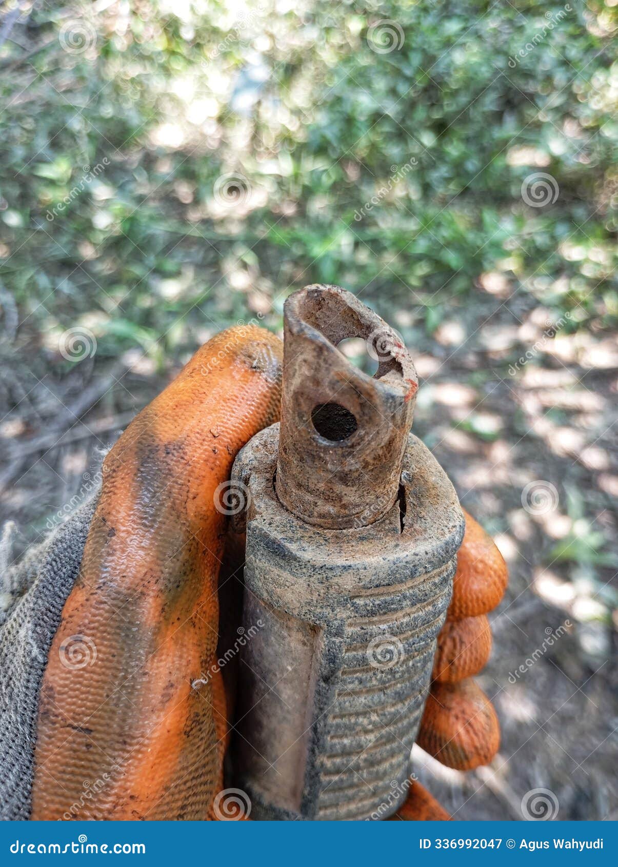 a close-up of a gloved hand holding a rusty, damaged object, possibly a pipe or a tool handle. the object is partially buried