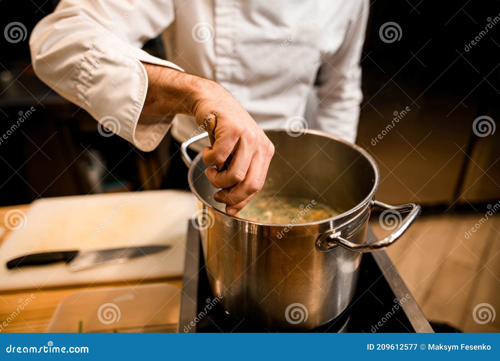 Chef stirring soup in large pot on stove available as Framed