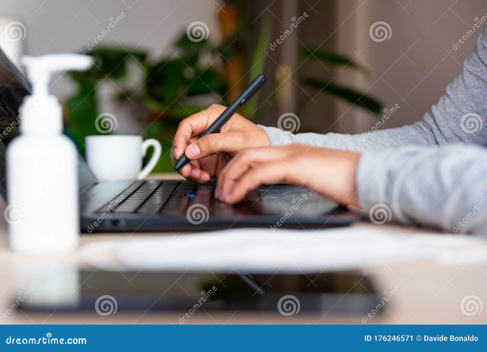 close up of hands of young woman typing on laptop keyboard with hand sanitizer while remote working due to corona virus spread