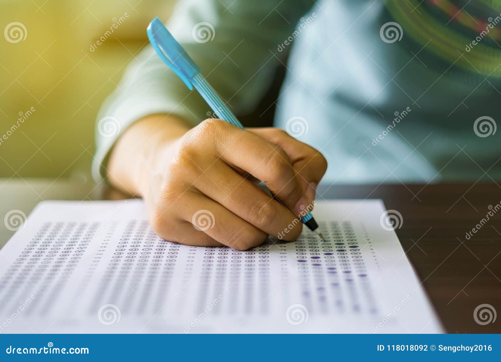 close up of high school or university student holding a pen writing on answer sheet paper in examination room. college students an