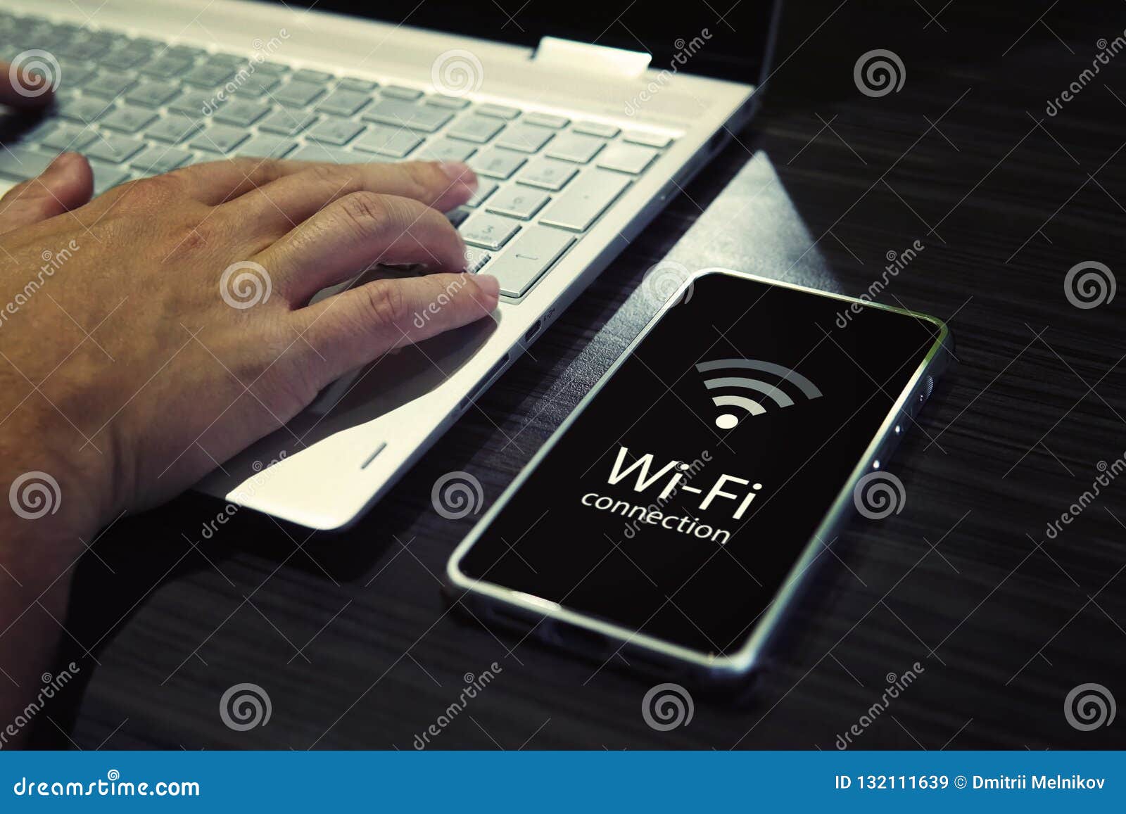 close up of male hands typing on laptop keypad and checking the smartphone wi-fi connection. cellphone with signal icon