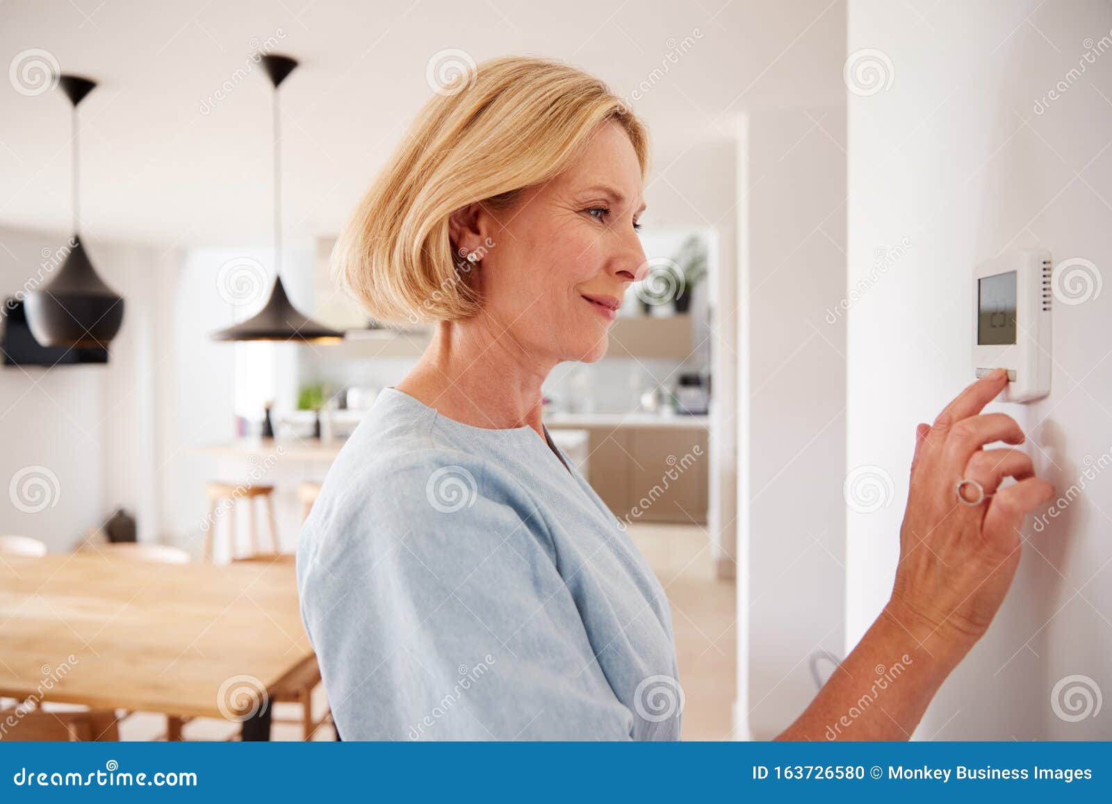 close up of mature woman adjusting central heating temperature at home on thermostat