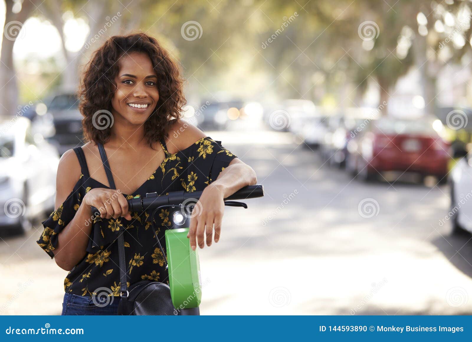 close up of millennial african american  woman leaning on an electric scooter in the street, smiling to camera