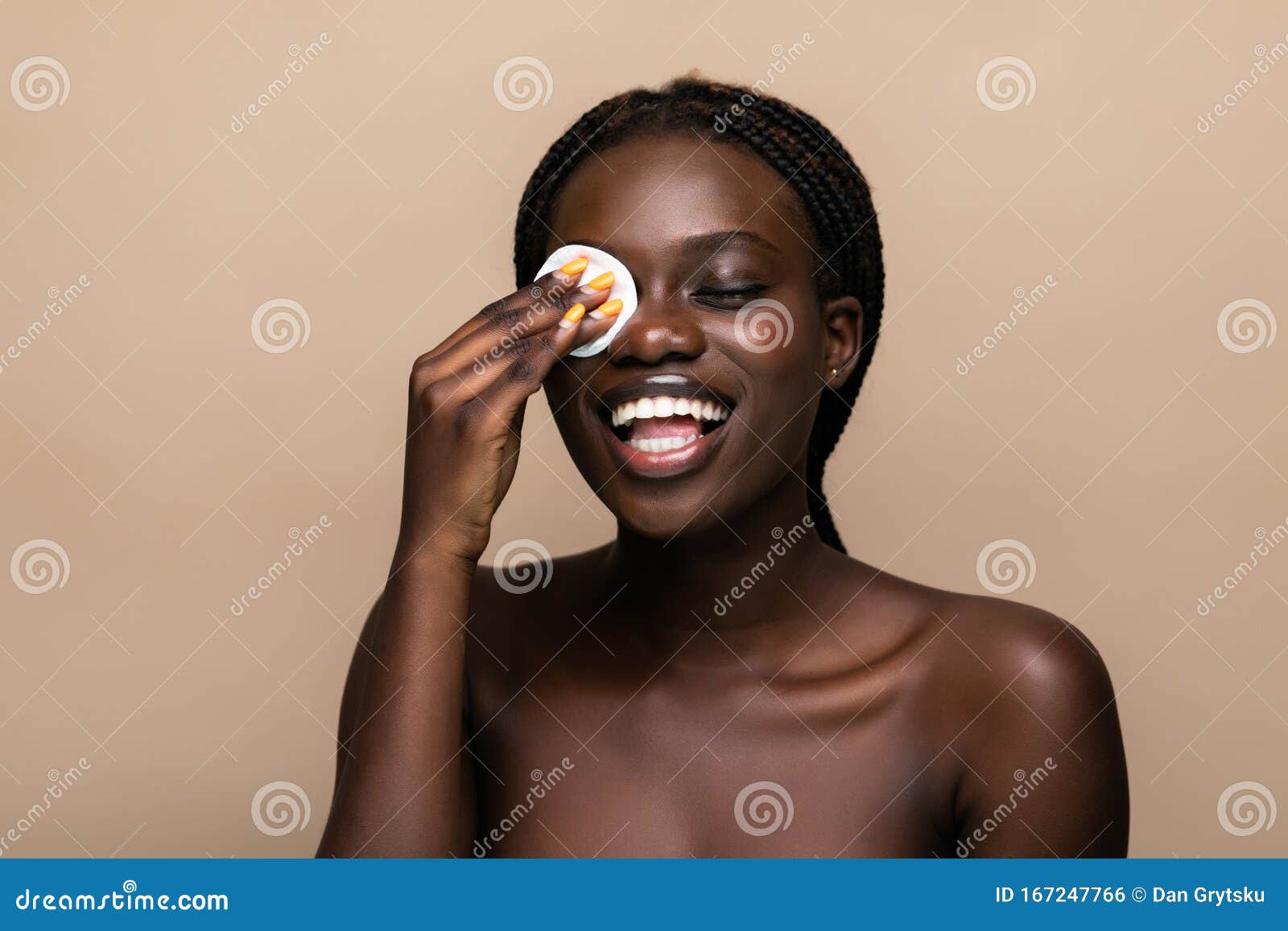 close up portrait of an attractive african american woman removing makeup with sponge  on beige background