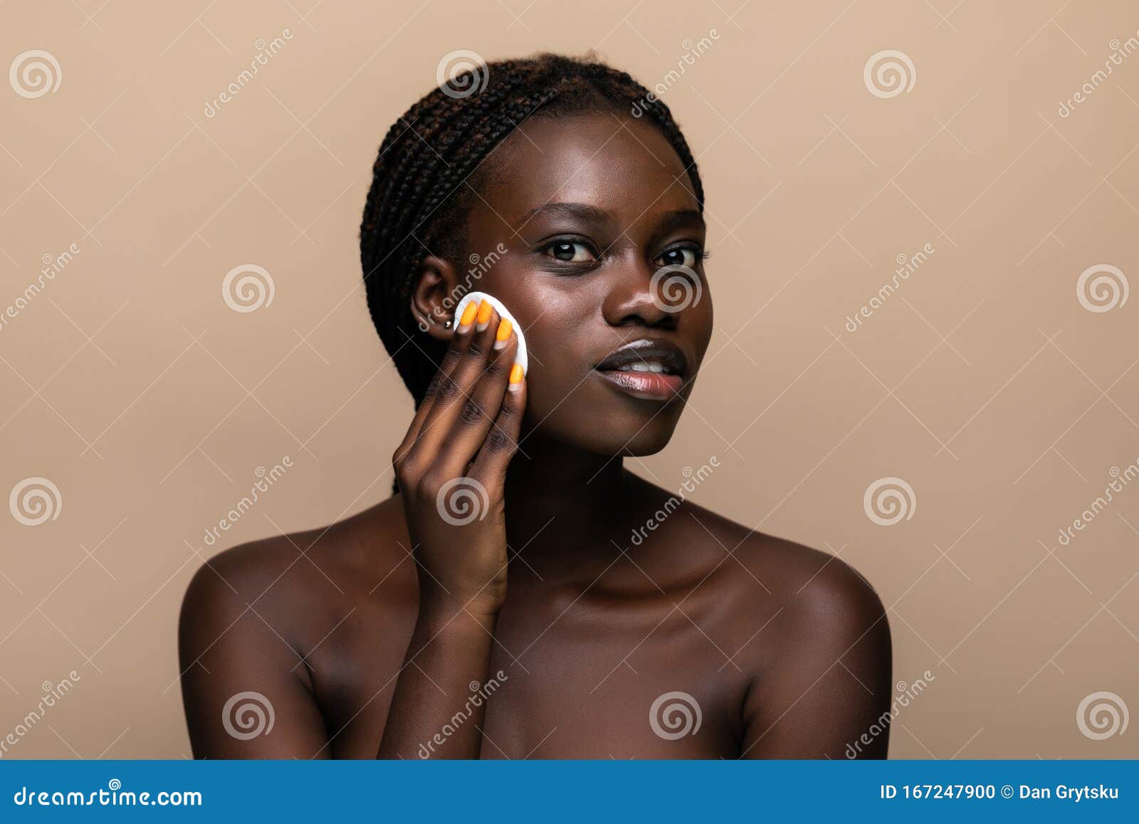 close up portrait of an attractive african american woman removing makeup with sponge  on beige background
