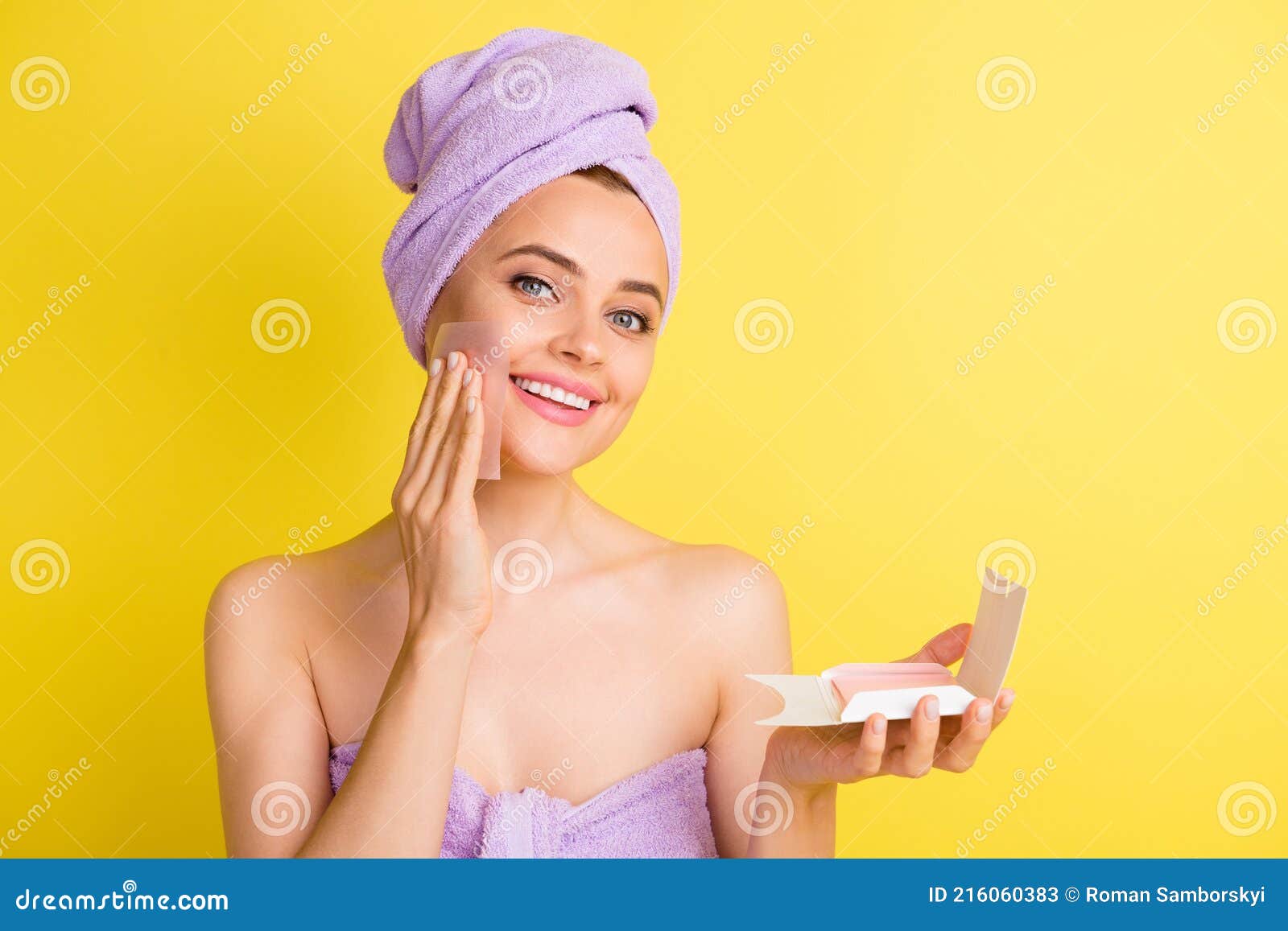 close-up portrait of charming cheery girl wiping oily skin with napkin  over vibrant yellow color background