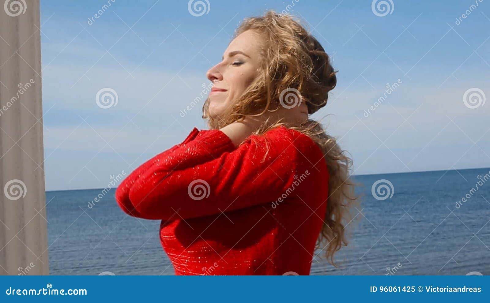 Close Up Portrait Of Woman Running Hand Through Curly Hair Blowing In Wind By Sea On Beach 