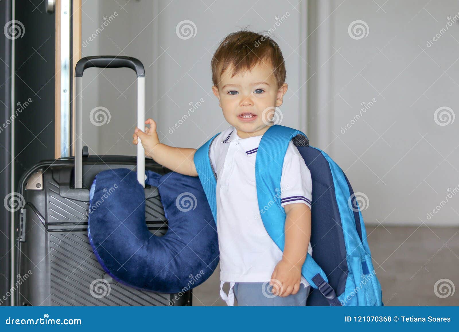 close-up portrat of cute smiling little baby boy with big backpack and suitcase with travelling pillow stay near open door ready t