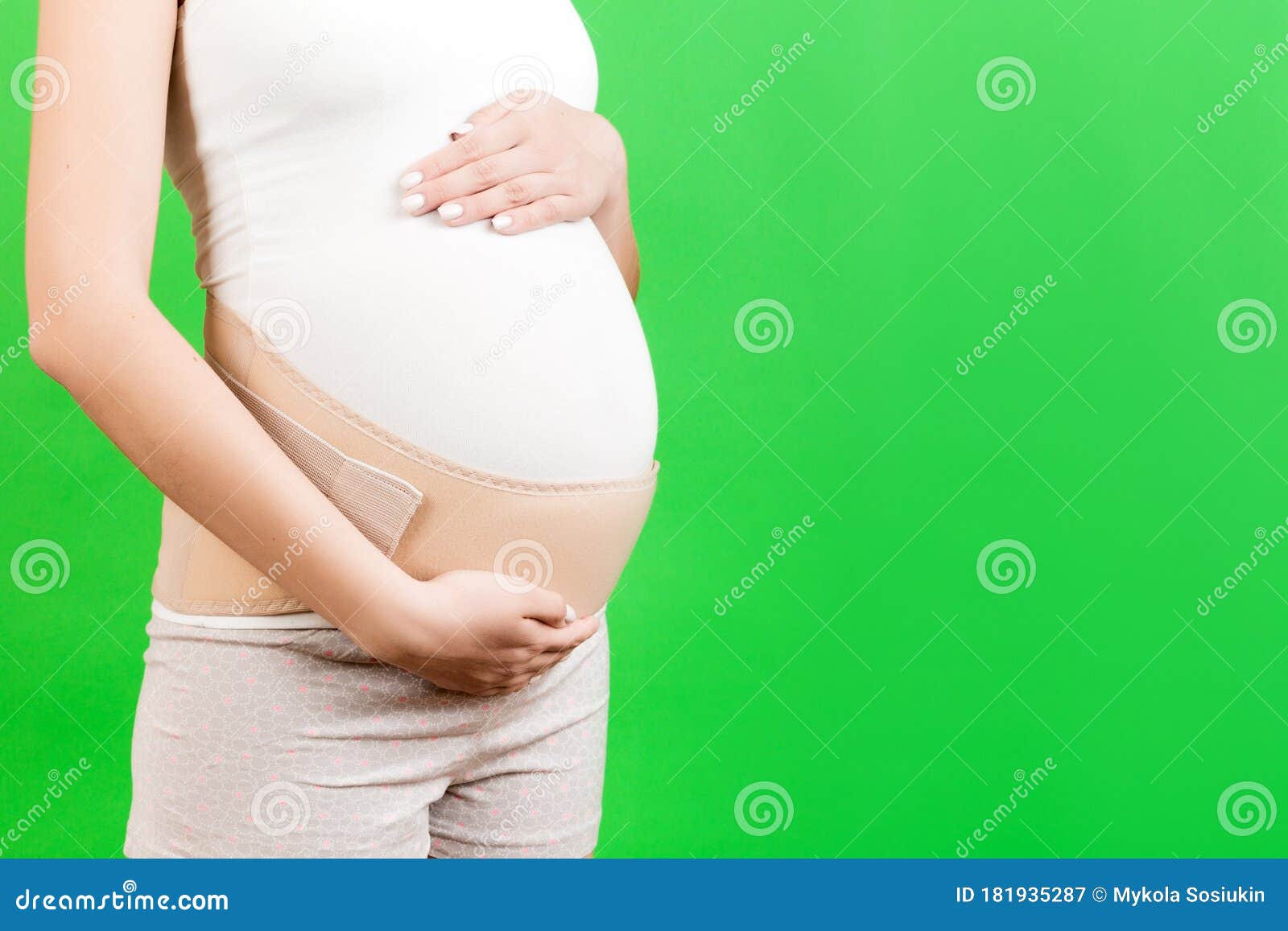 close up of pregnant woman dressed in orthopedic corset for reducing pain in the back at green background with copy space.