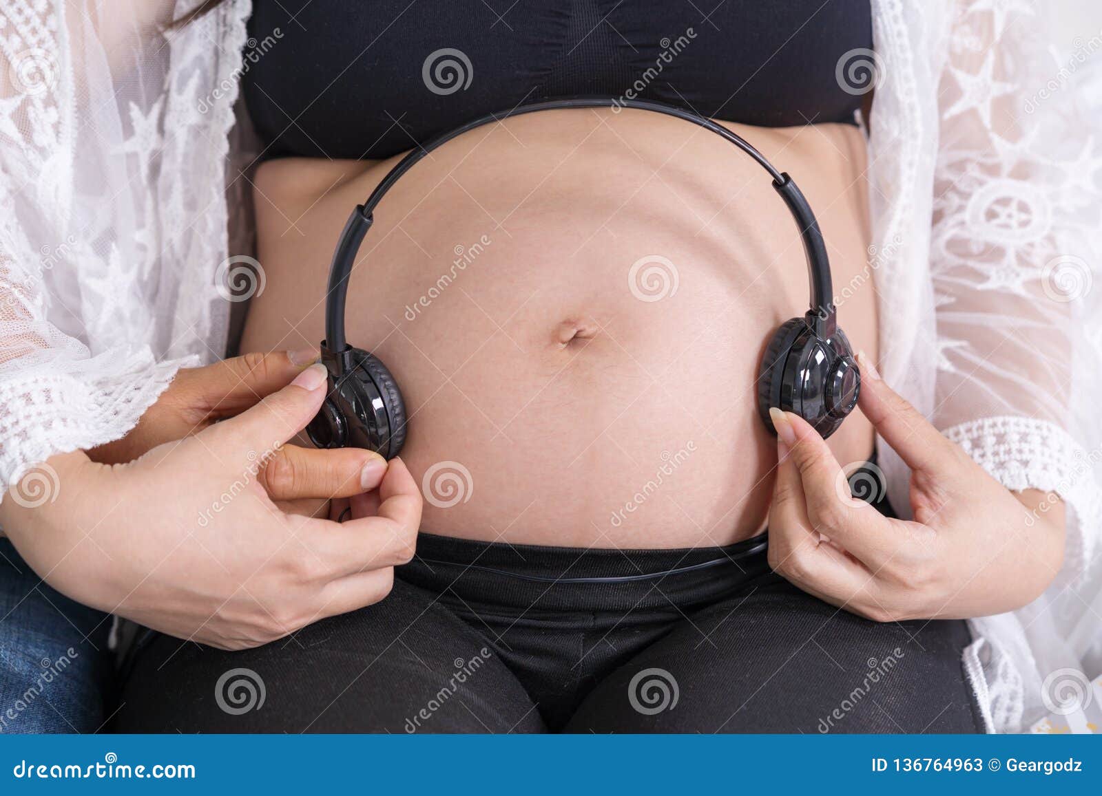 Woman with headphones on pregnant belly Stock Photo by ©Voyagerix 183453360