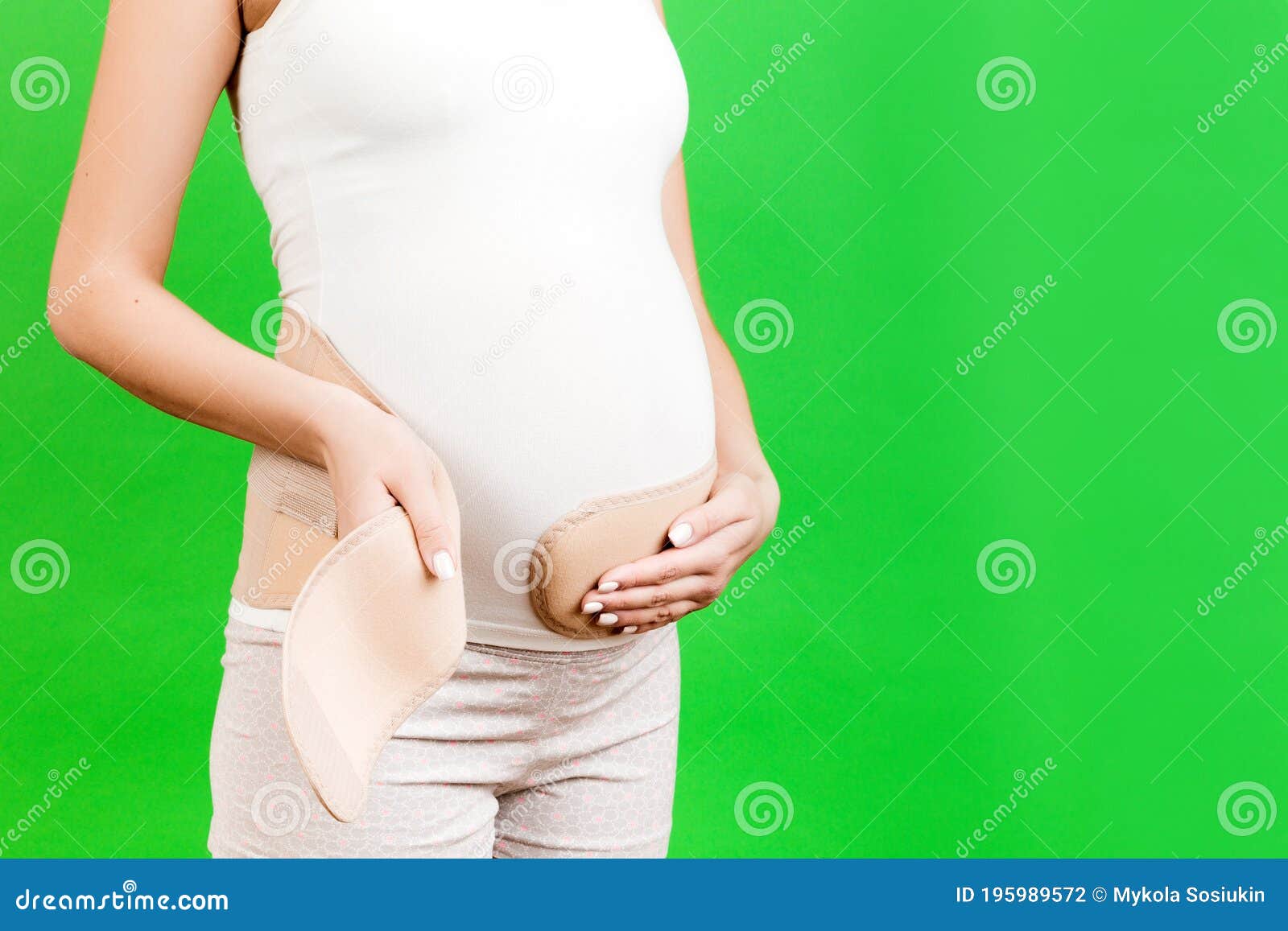 Close Up Of Pregnant Woman Putting On Maternity Belt On Her Belly At 