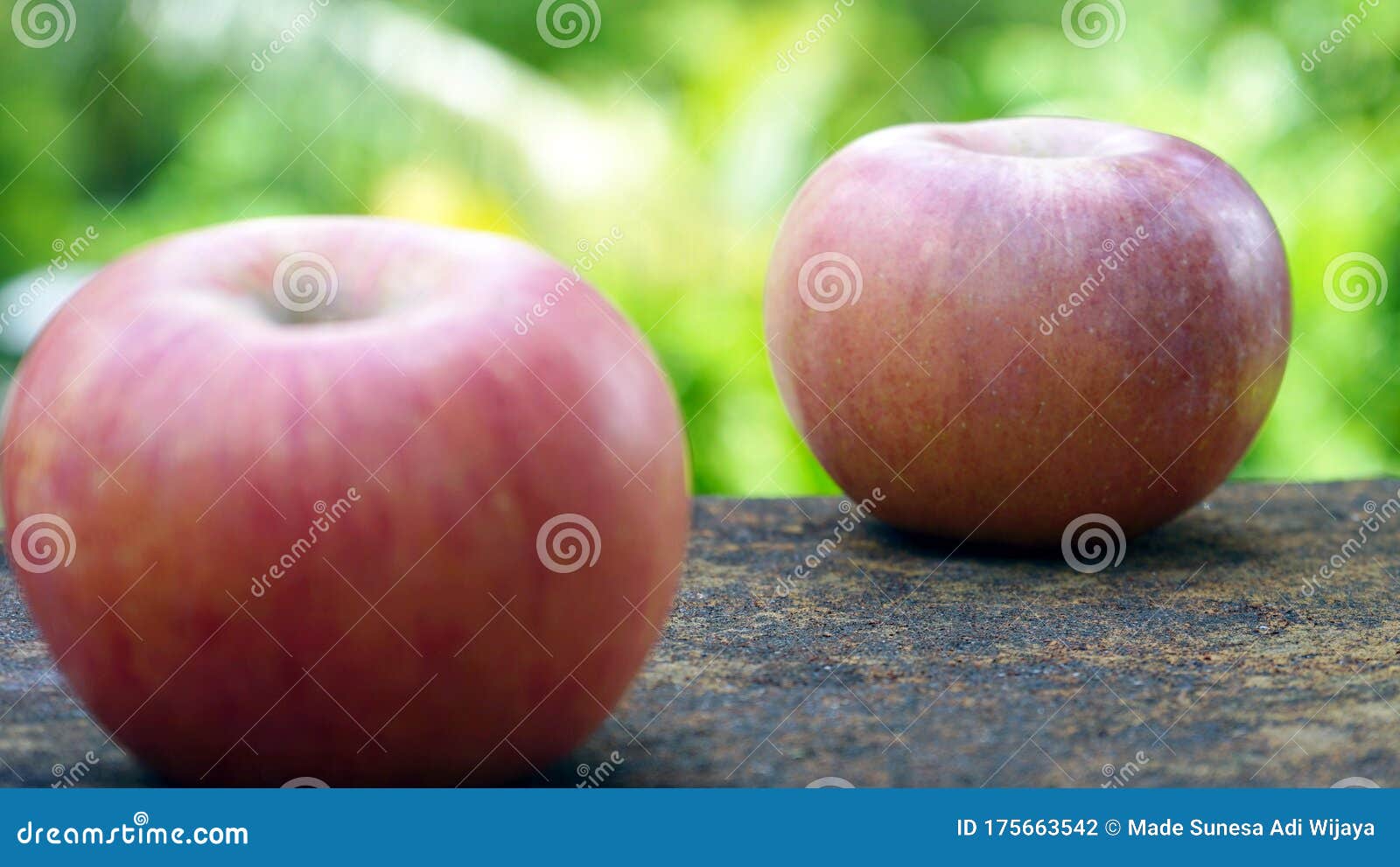 close up of a red apple on a table with a background of leaves