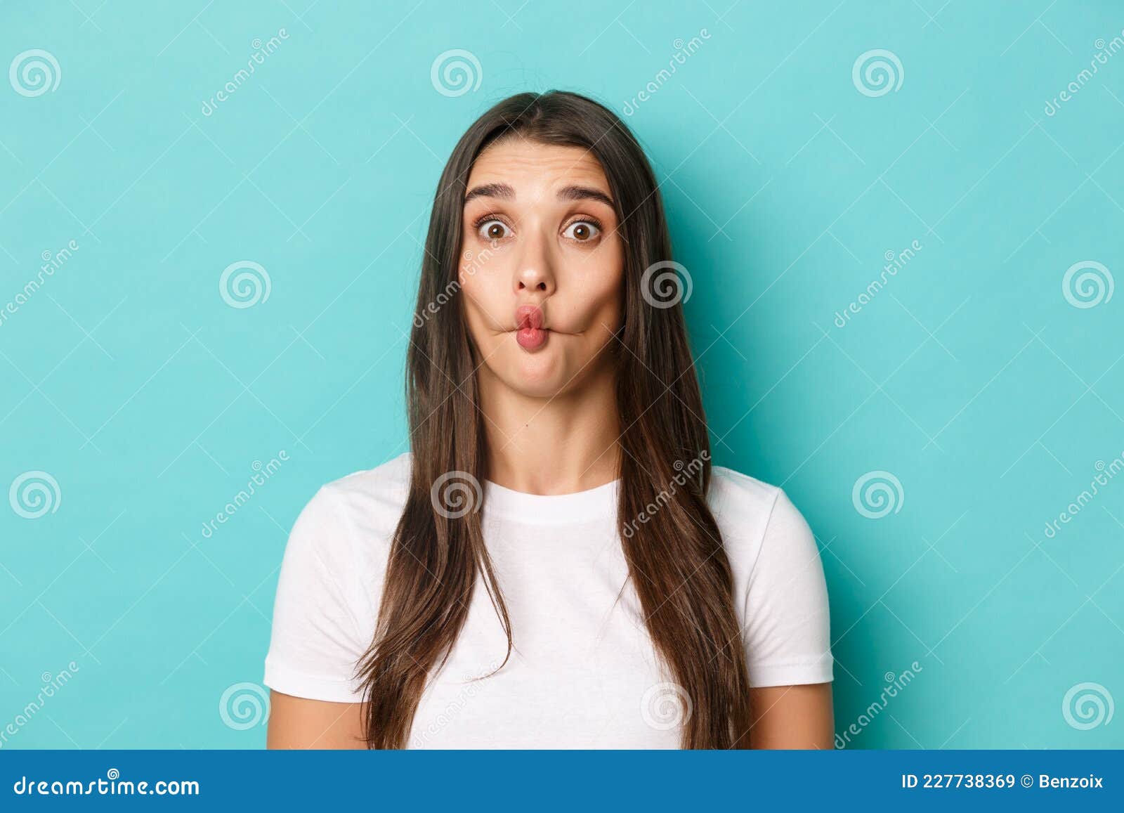 Close Up Of Silly Brunette Woman Sucking Lips And Showing Funny Faces Standing Over Blue