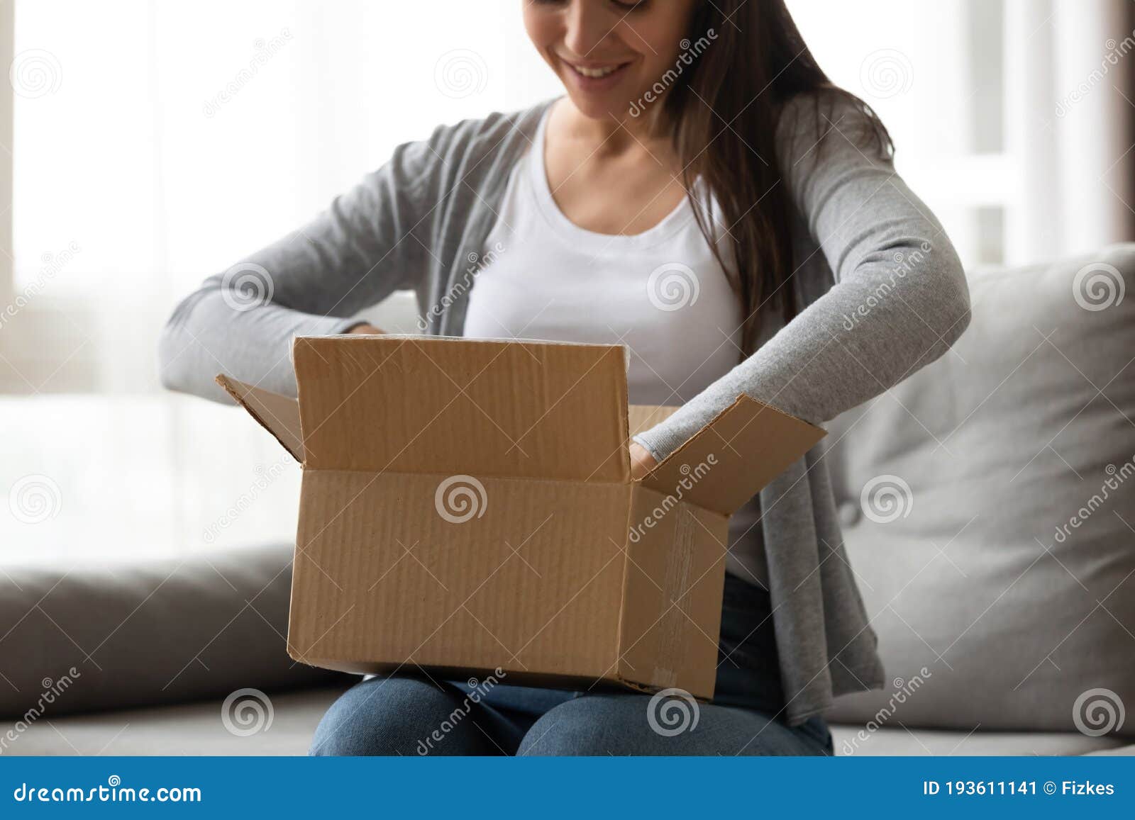happy young woman unboxing cardboard parcel at home.