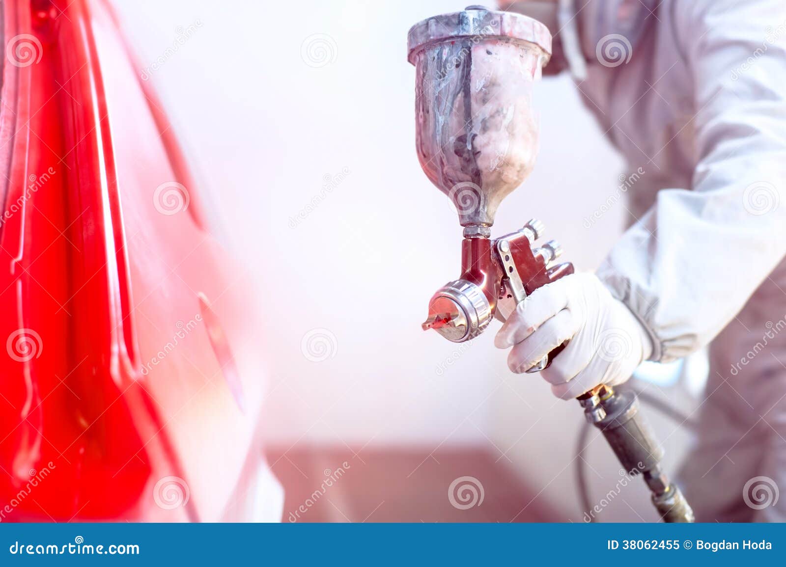 close-up of spray gun with red paint painting a car