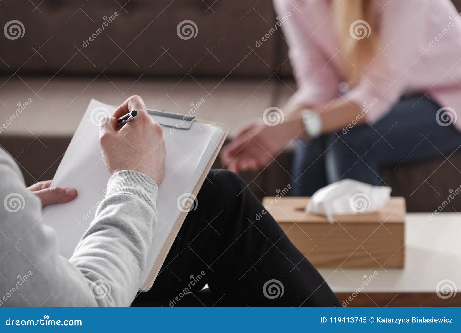 close-up of therapist hand writing notes during a counseling session with a single woman sitting on a couch in the blurred