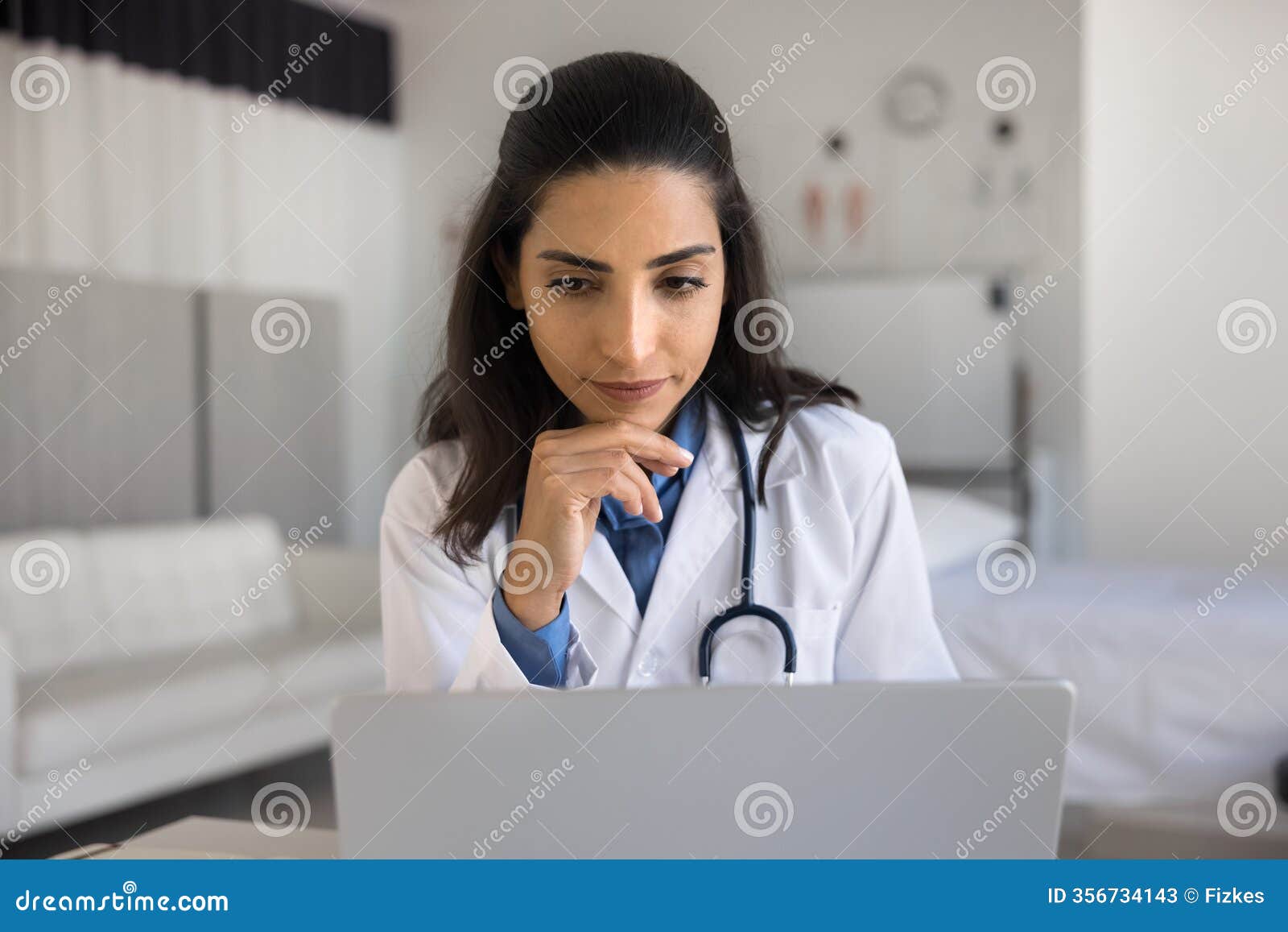 close up of thoughtful brazilian doctor using laptop at workplace