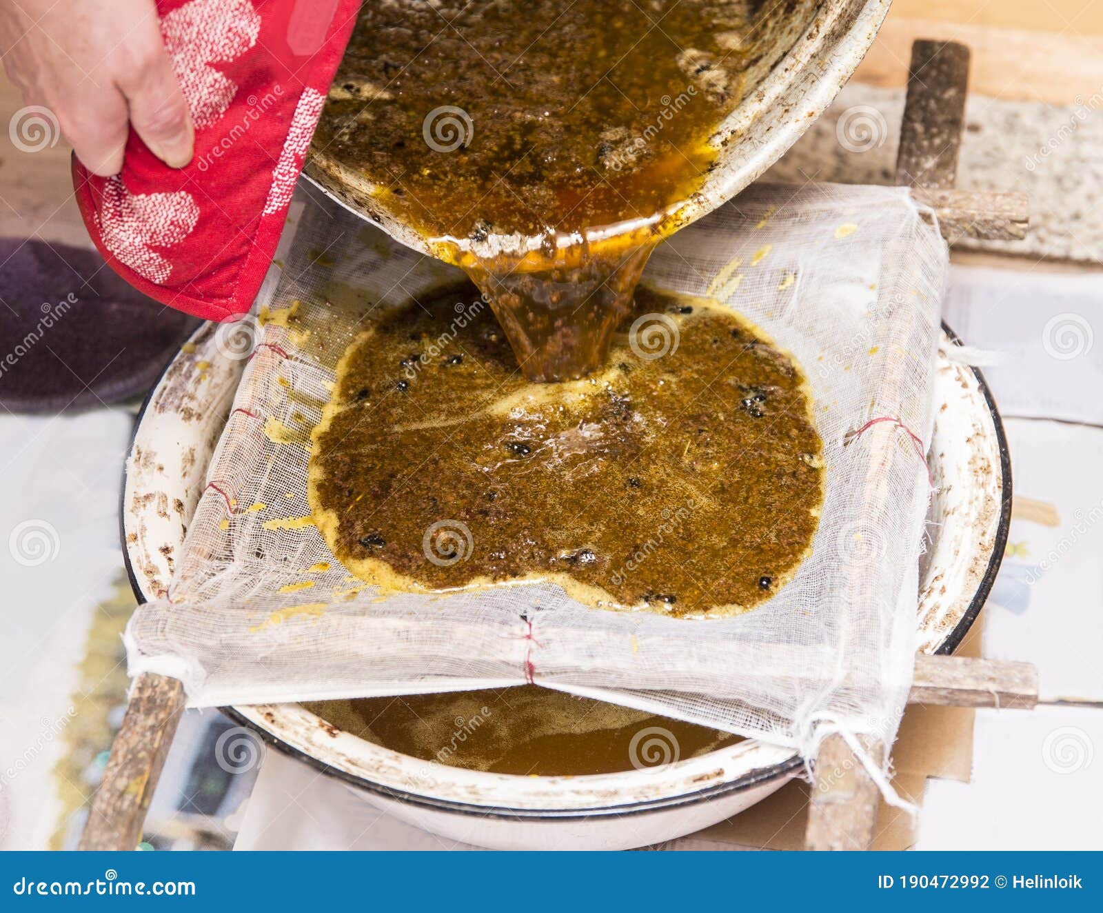 close up view of beekeeper pouring melted beeswax cera alba through gauze filter to clean old used wax and reuse it.