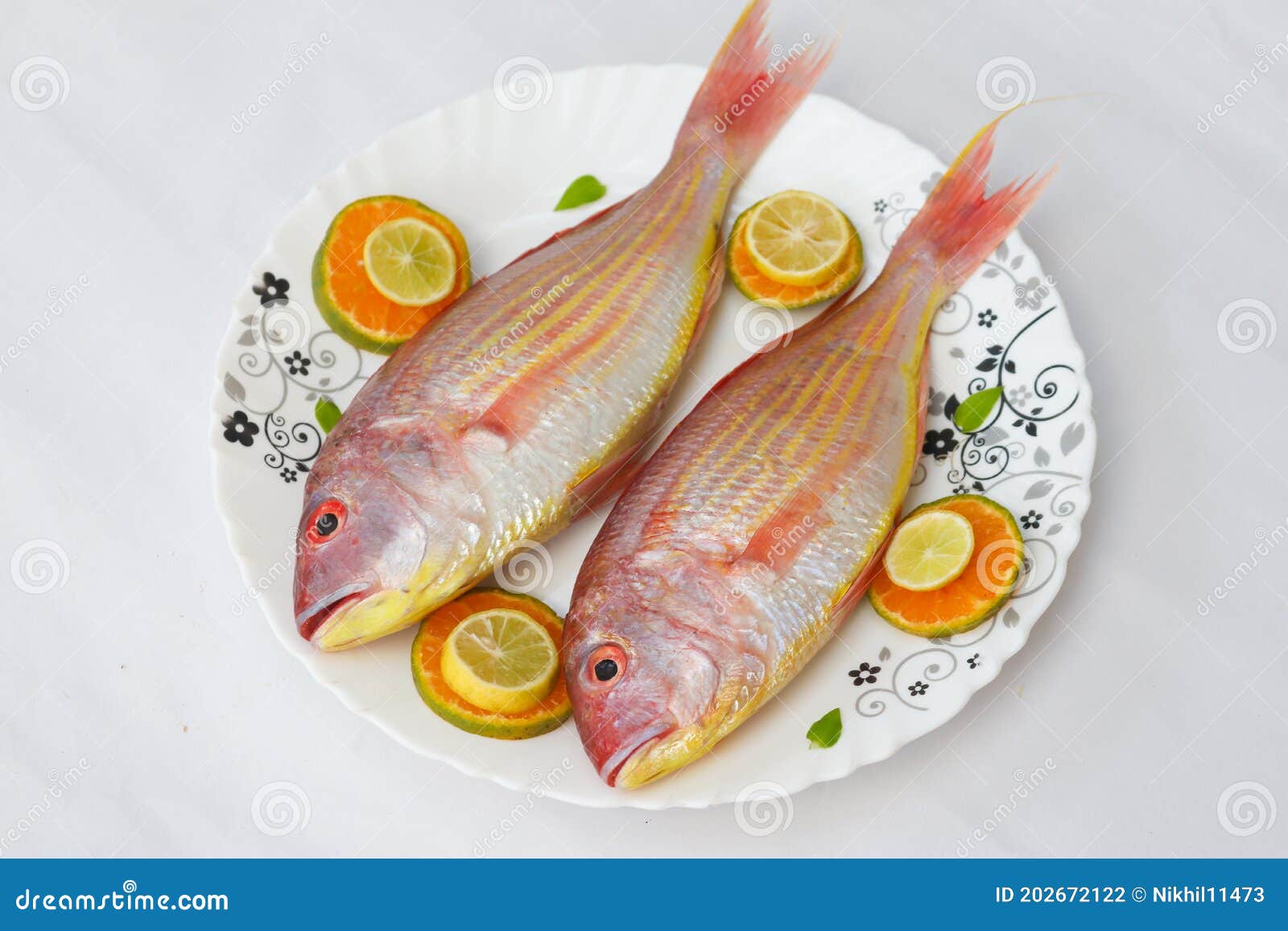 close up view of fresh pink perch (thread finned bream) decorated with lemon slice orange slice and curry leaves