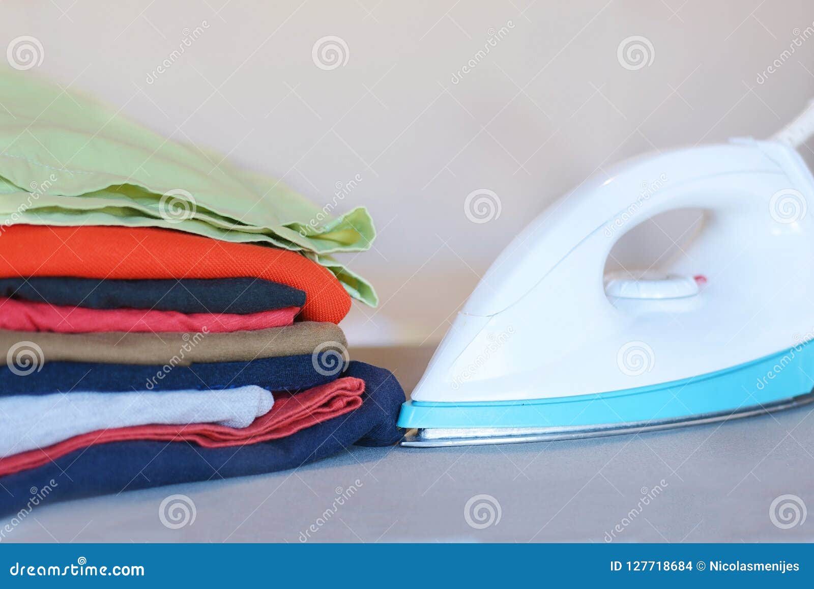 Close Up View of Iron Clothes on Ironing Board with Stack of Ironed Shirts Stock Photo Image