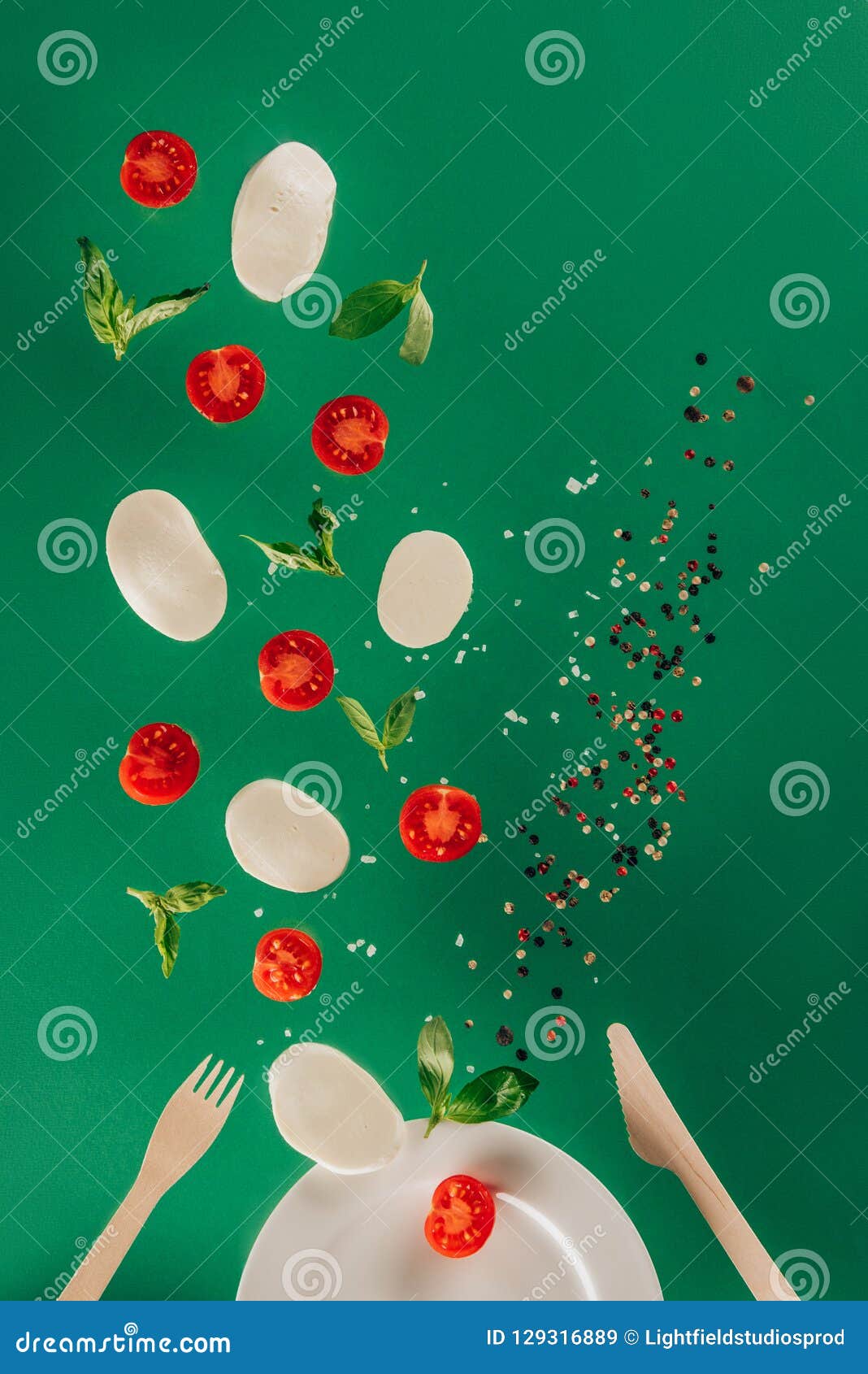 close up view of mozzarella cheese cherry tomatoes spinach and spices falling on plate