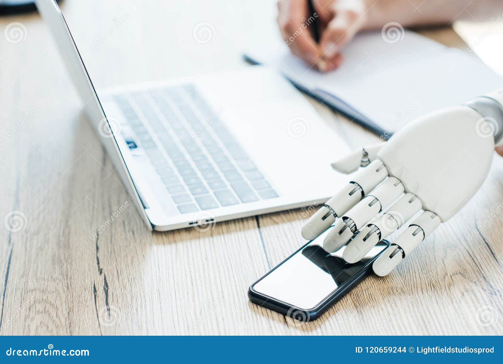 close-up view of robot hand using smartphone and human hand taking notes at workplace