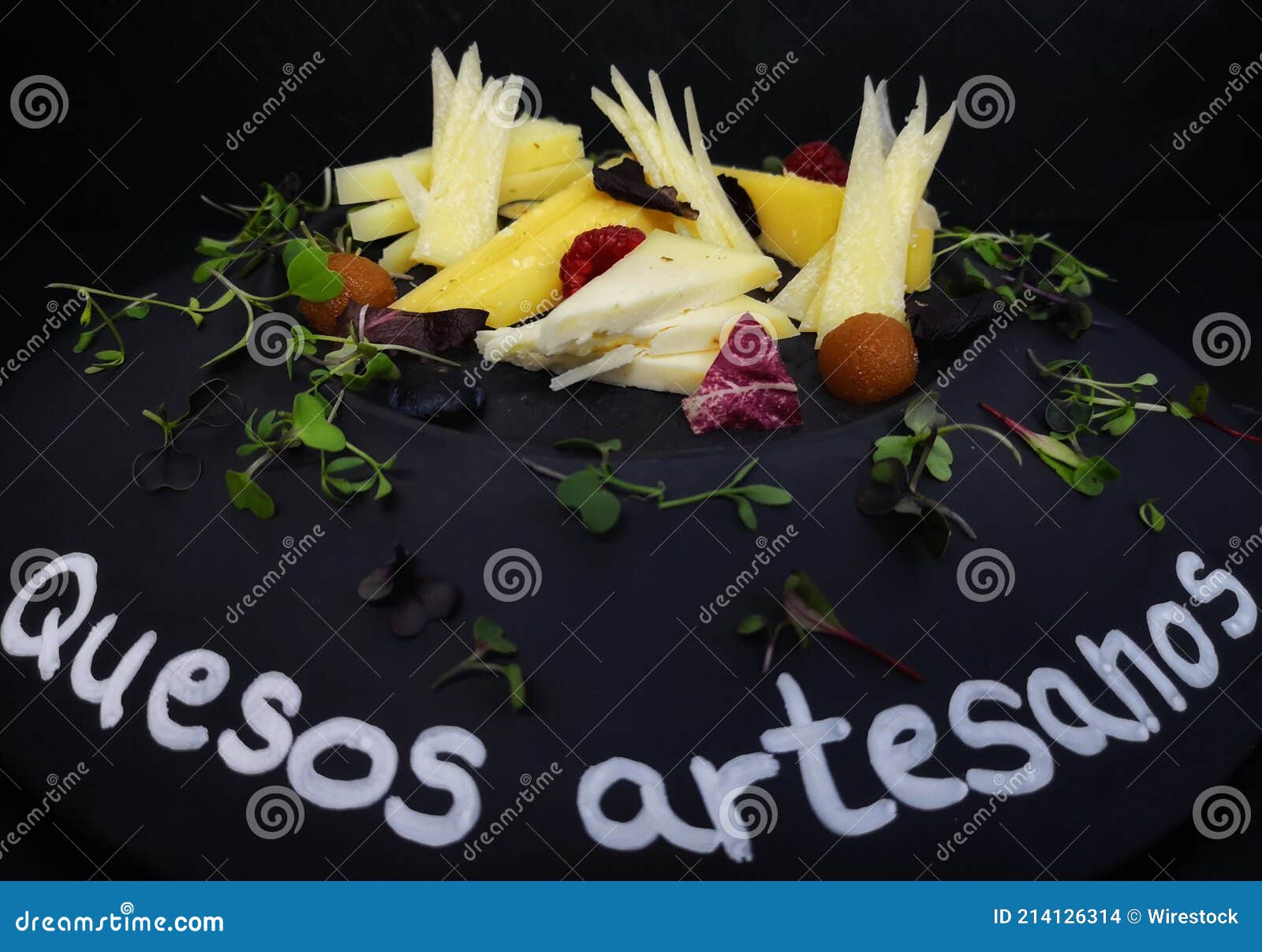 closeup of artisan cheese on a black plate with herbs and spanish text quesos artesanos