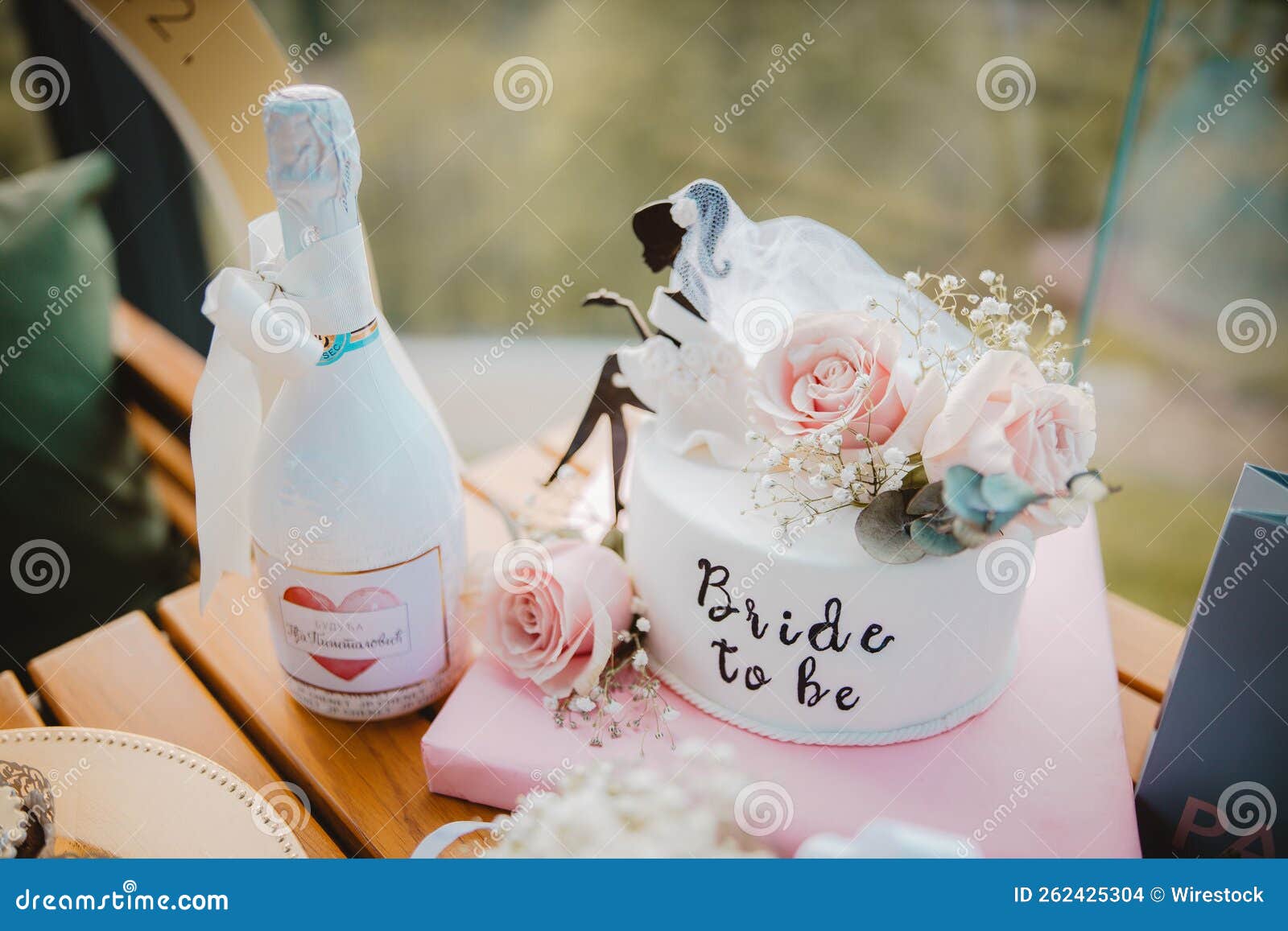 closeup of a bottle of champagne and a cake decorated with pink roses for 'bride to be' party